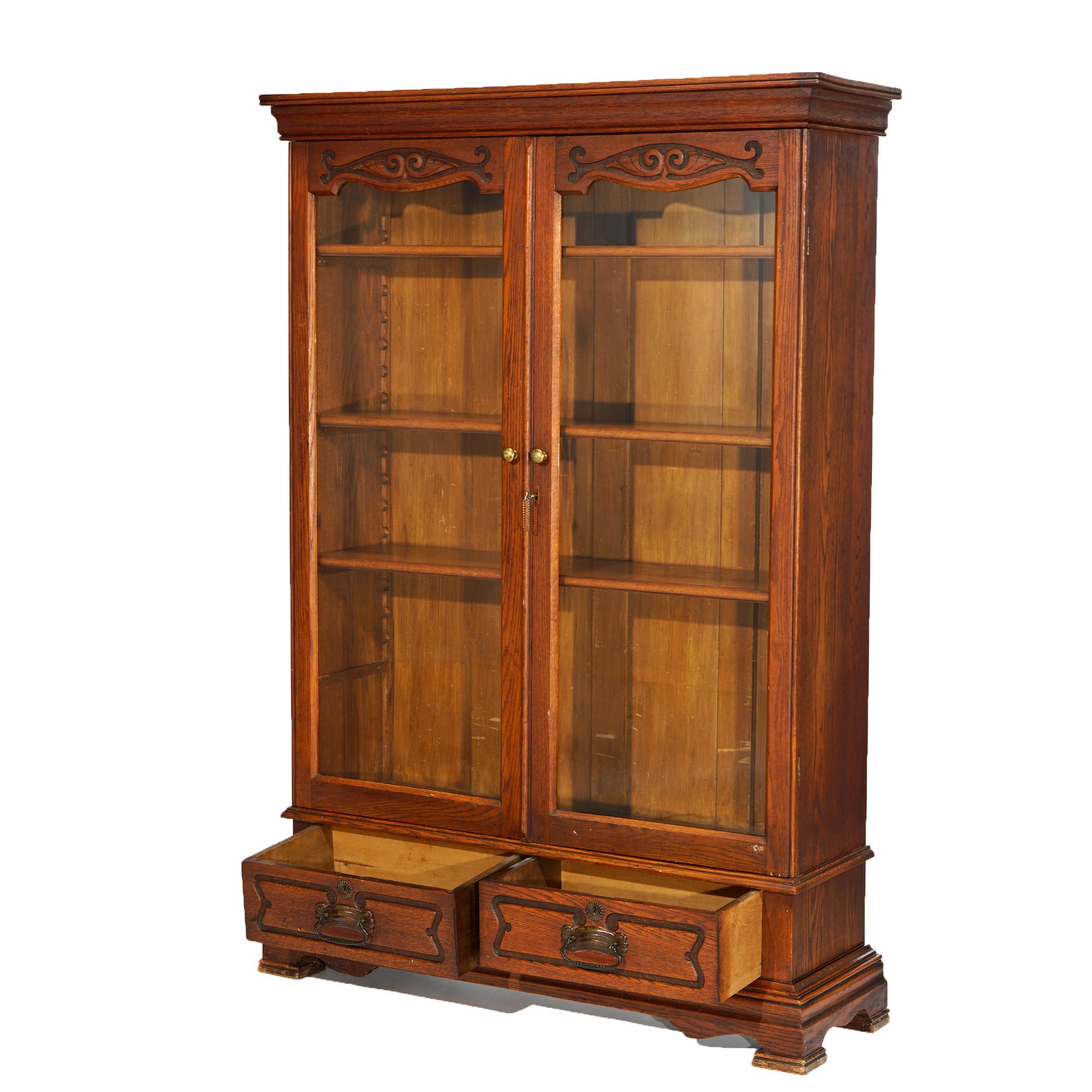 An antique Arts and Crafts Mission bookcase offers oak construction with double glass doors having carved scroll and foliate crests opening to shelved interior and raised on bracket feet, elements of Art Nouveau, c1910

Measures- 63.25''H x 44''W x