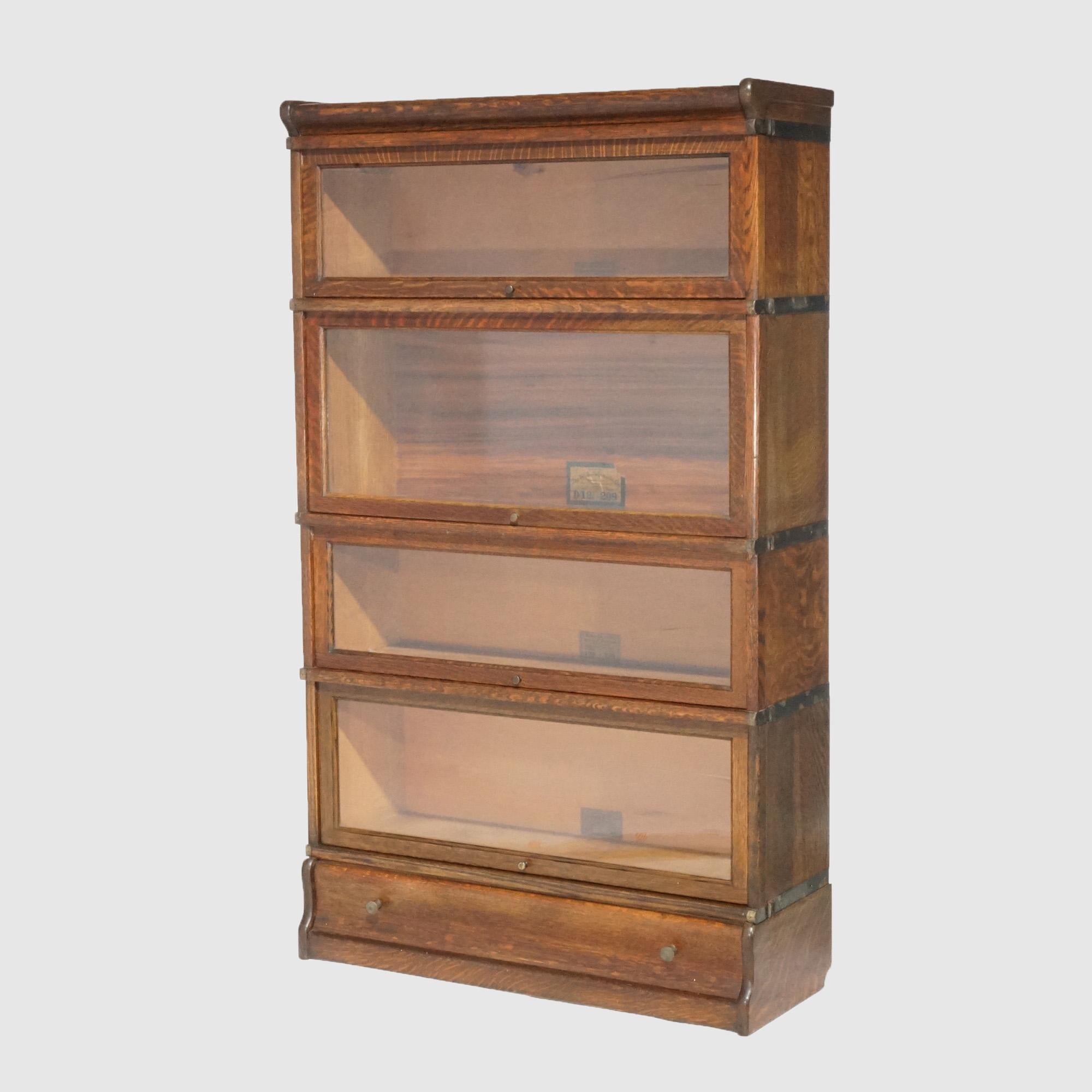 Un'antica libreria barrister Arts and Crafts di Globe Wernicke offre una struttura in quercia con quattro pile, ognuna delle quali ha cassetti estraibili, e poggia su una base a ogiva con un singolo cassetto lungo, etichette del produttore come da