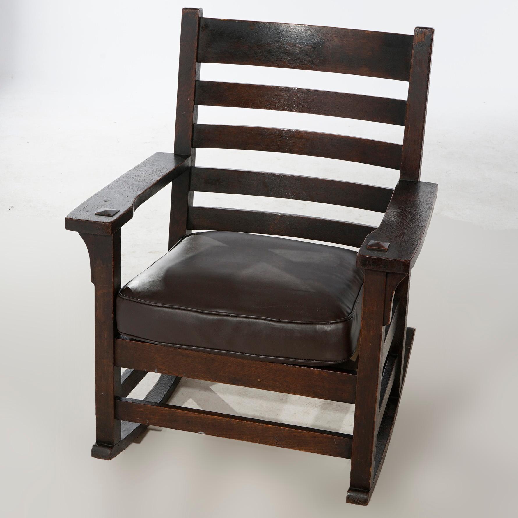 An antique Arts and Crafts Gustav Stickley rocking chair offers quarter sawn oak construction with ladder back and upholstered seat, c1910.

Measures- 35''H x 27.25''W x 28.25''D.
