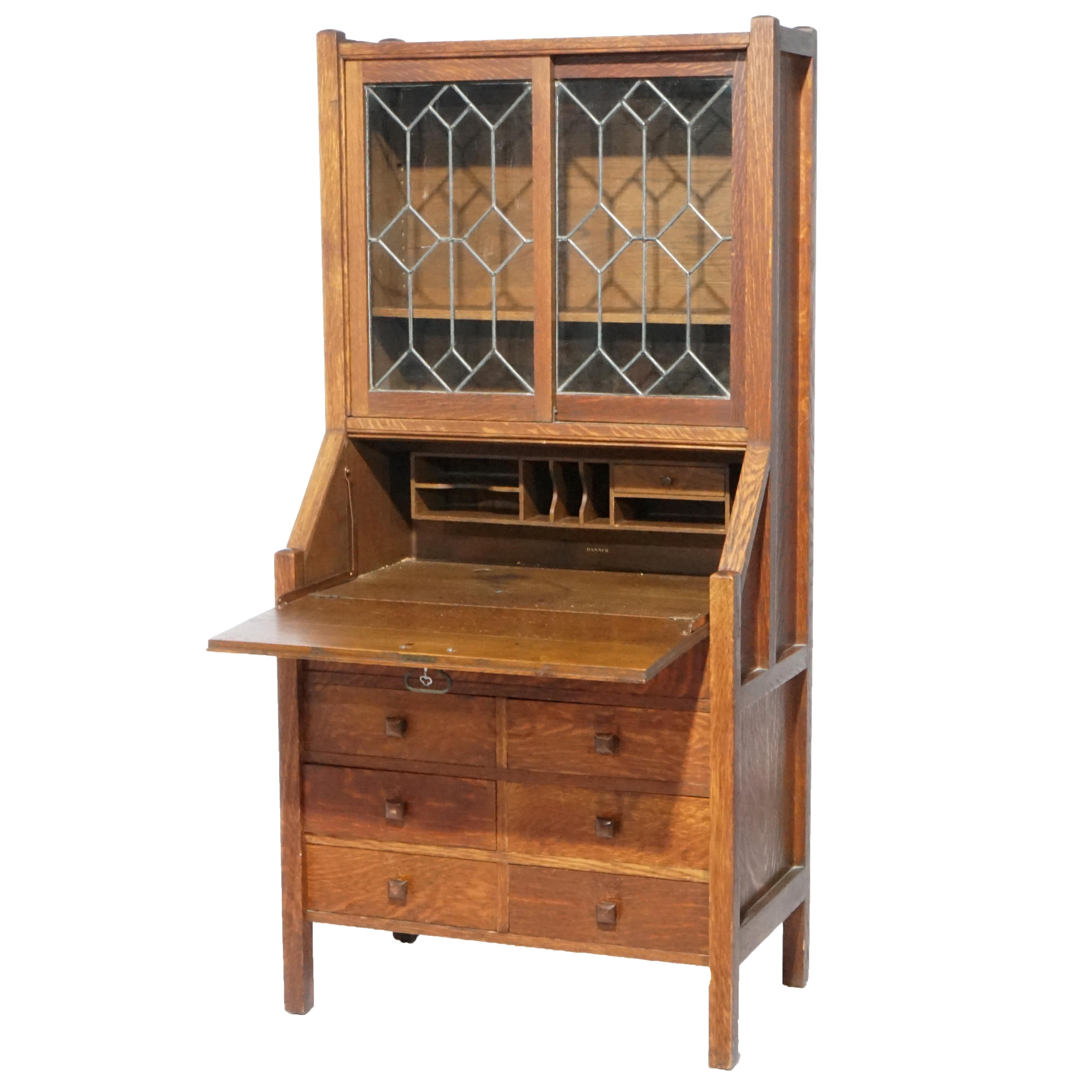 An antique Arts and Crafts Mission drop-front secretary offers quarter sawn oak construction with upper bookcase having double leaded glass doors opening to shelved interior over slant front desk and lower case having single long drawer over six
