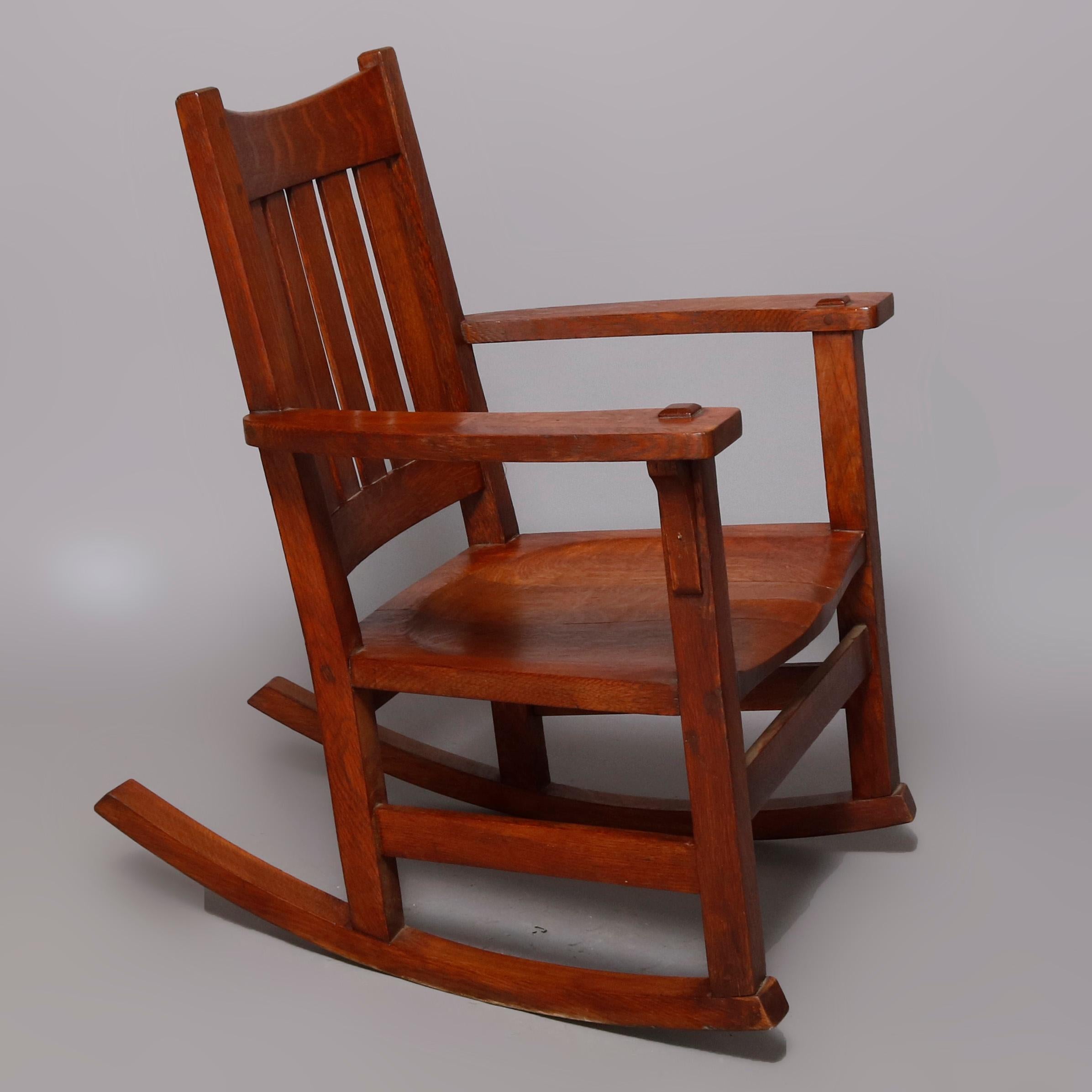 Une chaise à bascule Arts & Crafts ancienne offre une construction en chêne scié sur quartier avec un dossier à lattes et des bras mortaisés, marque du fabricant sous le bras, circa 1920.

Mesures : 28