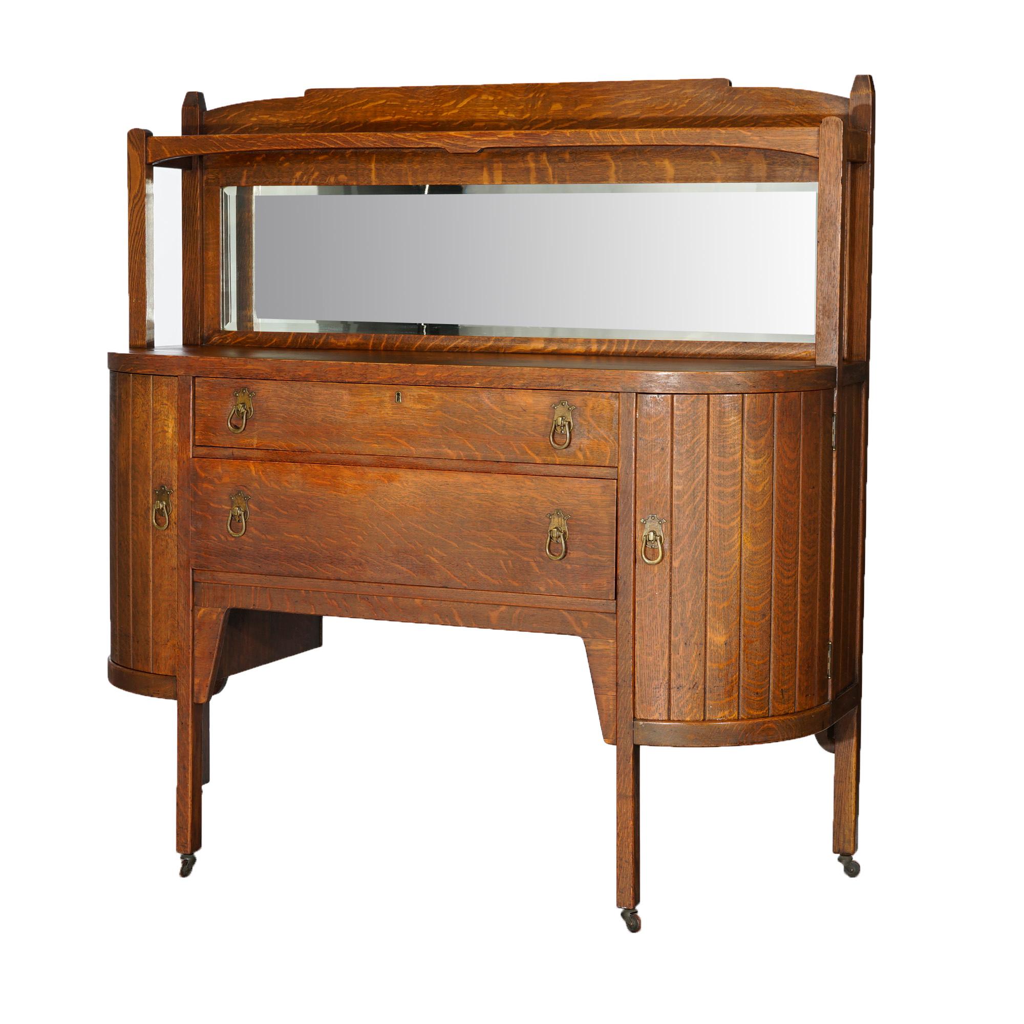 An antique Arts and Crafts Mission sideboard offers quarter sawn oak construction with mirrored backsplash having upper display over demilune form case with central drawer tower flanked by cabinets with slat from doors, raised on square and straight