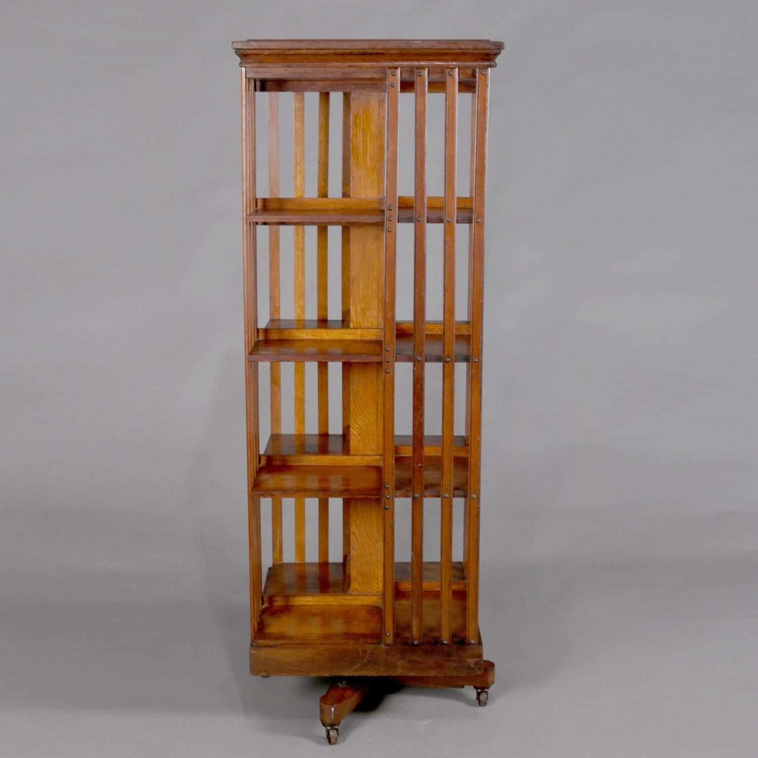 Antique Arts & Crafts Mission oak bookcase features square form with four shelves and slat sides, bookcase revolves and is seated on tripod base with wheels, Danner Trade Mark brand as photographed, circa 1910.

Measures - 55.5