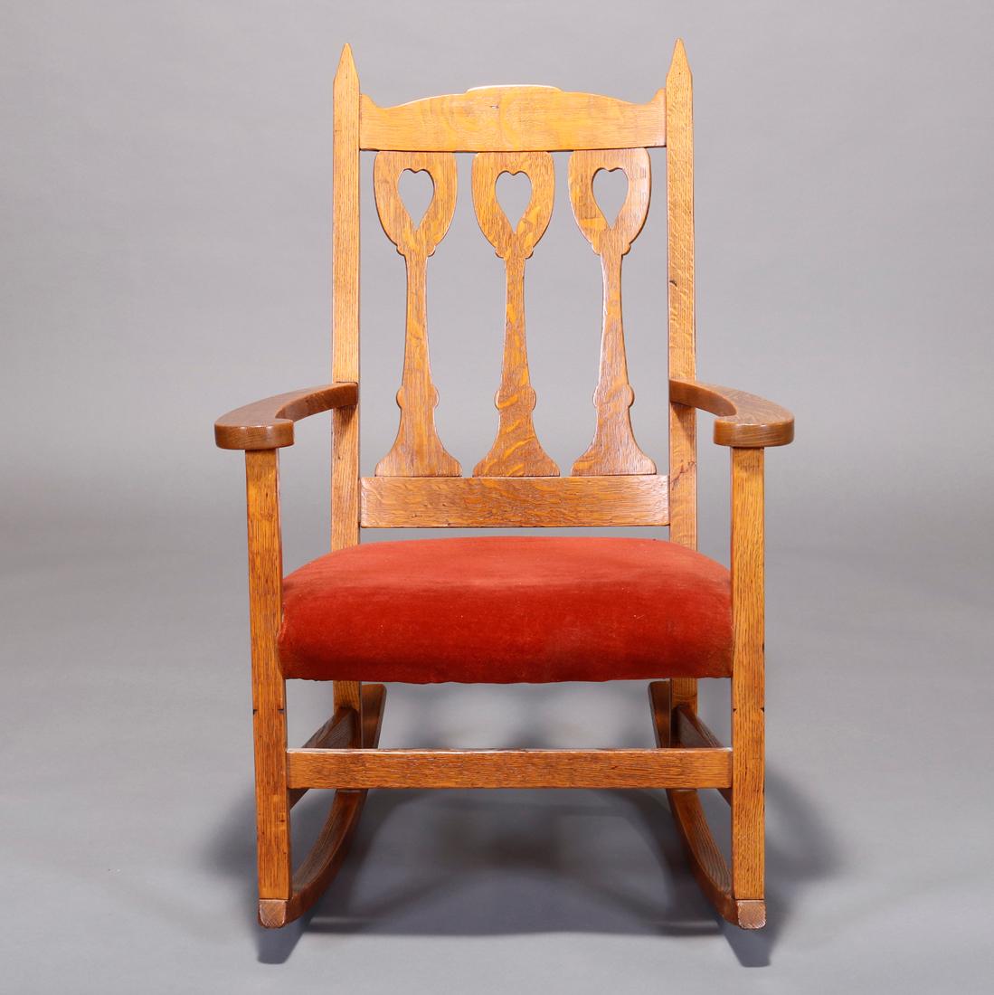 An antique Arts & Crafts Mission rocking chairs offers oak construction with back having stylized chalice form slats with cutout hearts over upholstered seat, c1910

Measures: 38.5