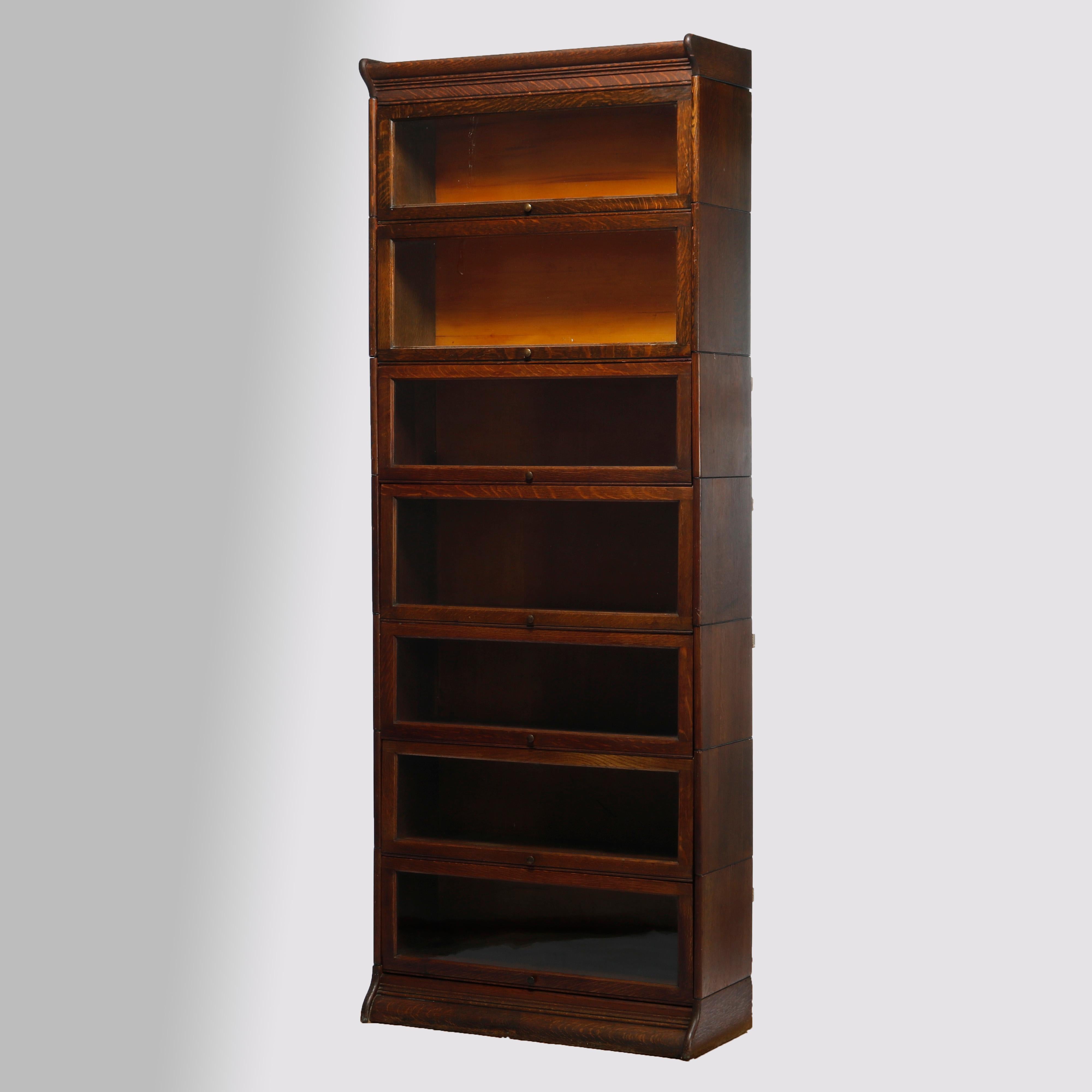 An antique Arts & Crafts Mission barrister bookcase in the manner of Globe Wernicke offers quarter sawn oak construction with seven stacks, each having pull-out glass doors, raised on ogee base, and having 