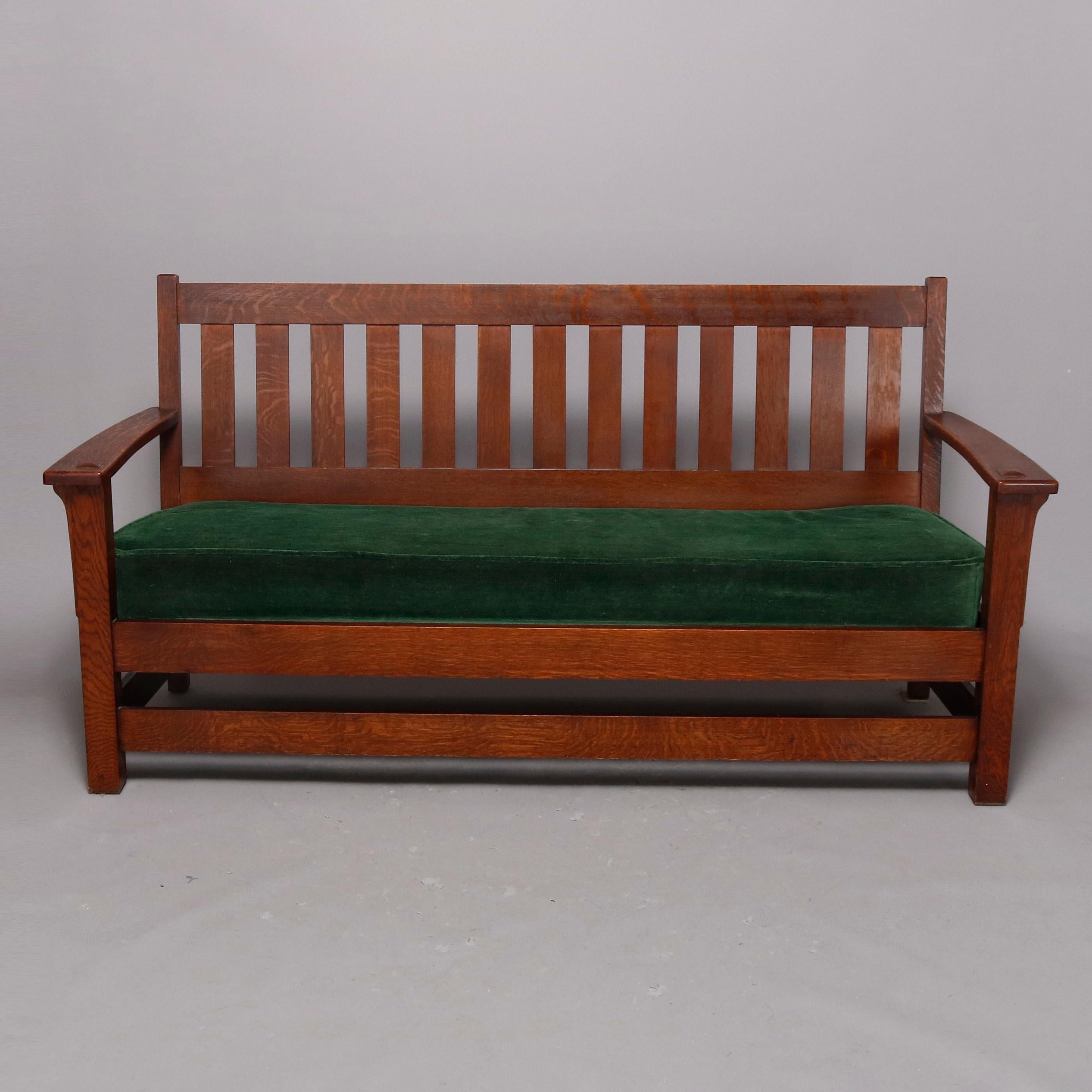 An Arts & Crafts mission oak settee by Limbert offers quarter sawn oak construction with slat back having double cushion surmounting cushioned seat flanked by open and mortised arms, brand stamp as photographed, circa 1910

Measures: 37