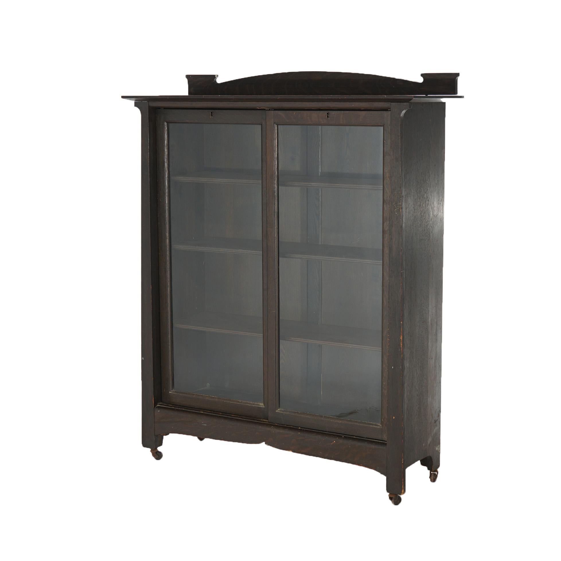 An antique Arts and Crafts Mission bookcase offers arched backsplash over case with sliding glass doors opening to shelved interior, c1910

Measures - 51.5