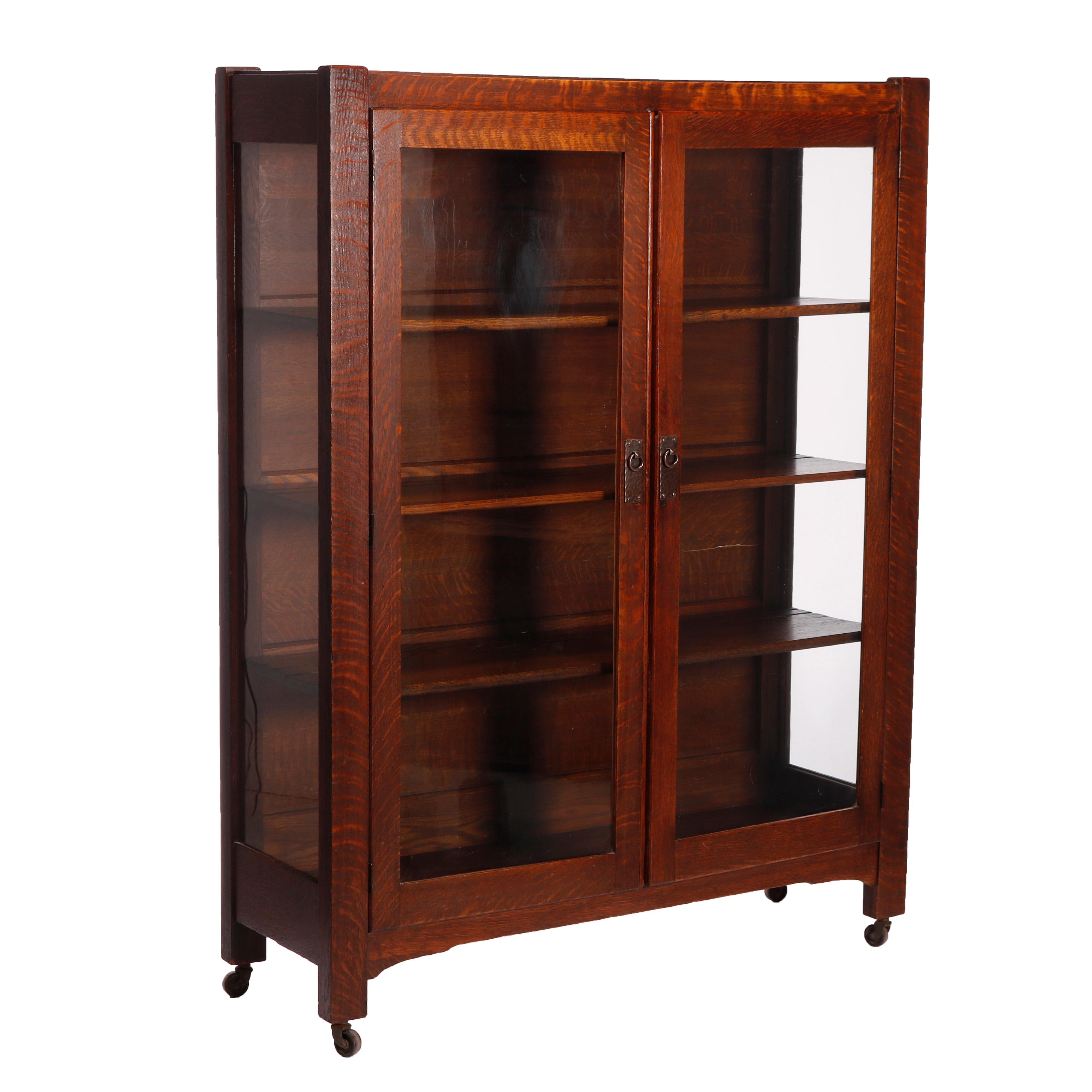 An antique Arts & Crafts Mission china cabinet in the manner of Stickley Bros. 
offers paneled quarter sawn oak construction with double glass doors opening to shelved interior, raised on straight square legs with casters, c1910

Measures -