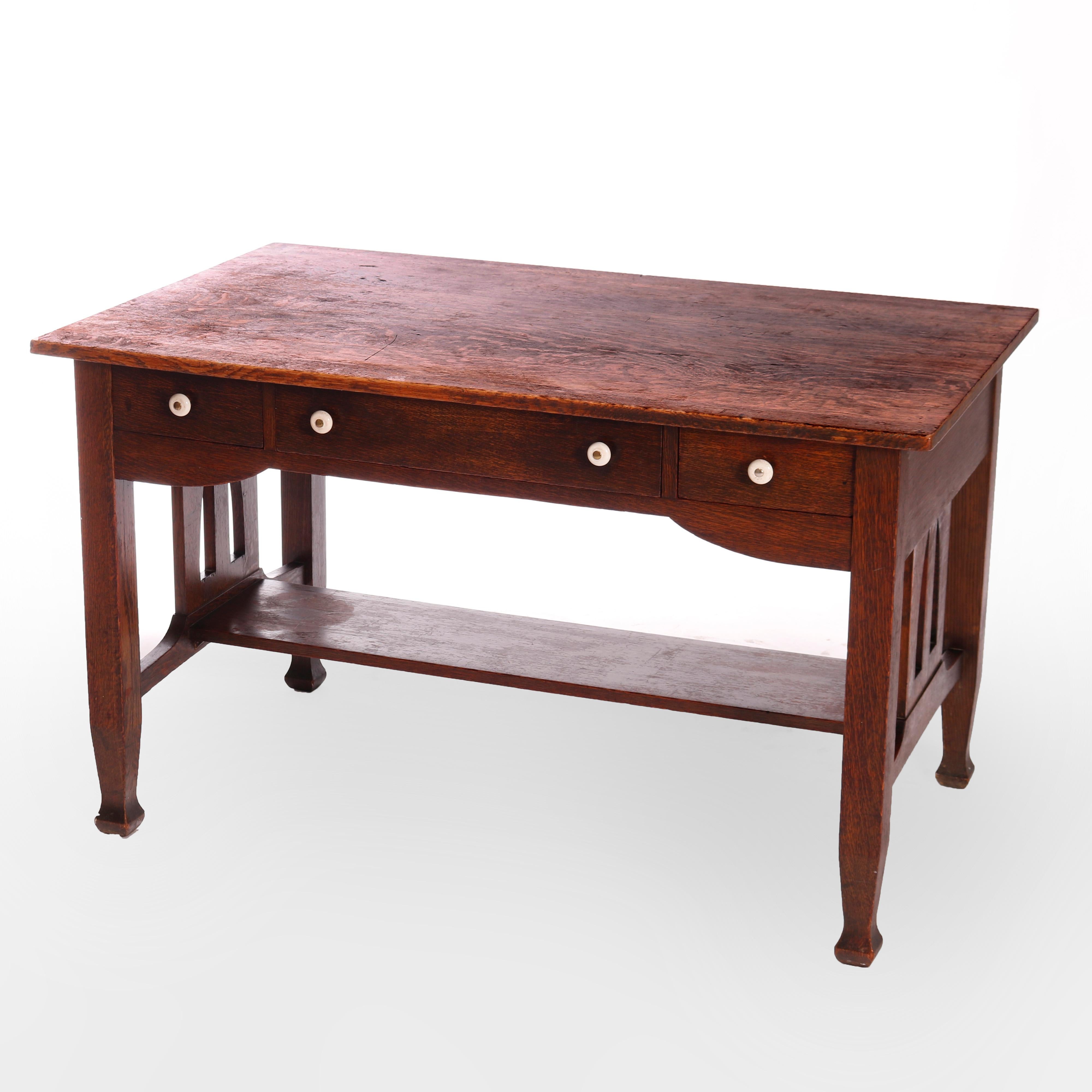 An antique Arts & Crafts library table by Bailey's offers quarter sawn oak construction with case having three drawers, raised on trestle base with cutout slat sides, lower shelf stretcher and Macmurdo feet, maker label as photographed,