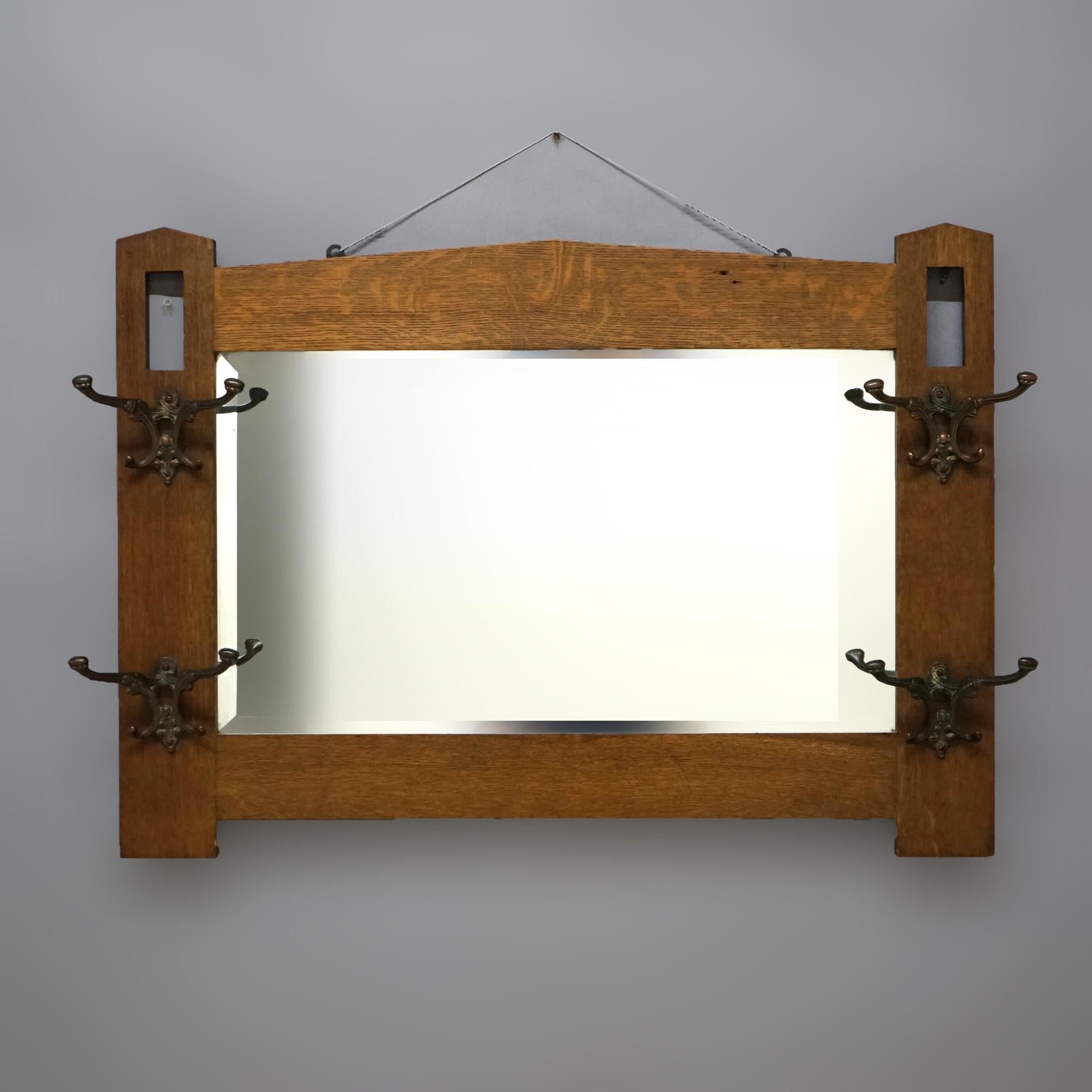 An antique Arts and Crafts Mission mirrored hat rack in the manner of Stickley offers quarter sawn oak frame with arched crest having flanking stylized columns with cutouts and foliate cast double hat hooks surrounding beveled mirror,