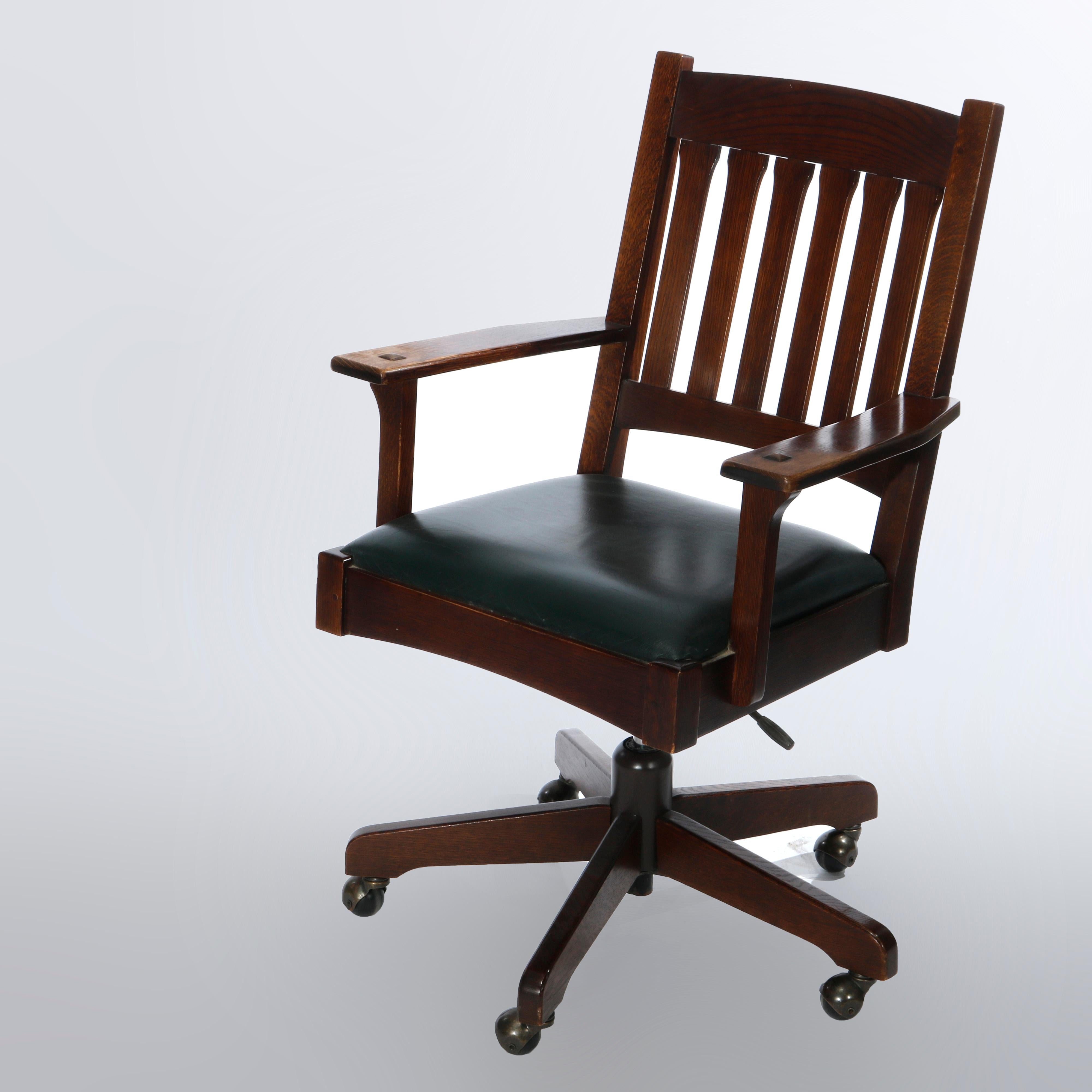 An Arts & Crafts Mission office chair in the manner of Stickely offers oak construction with slat back over covered seat and flat arms with pyramidal element at joint, swivel and telescoping rolling base, maker marks as photographed, 20th