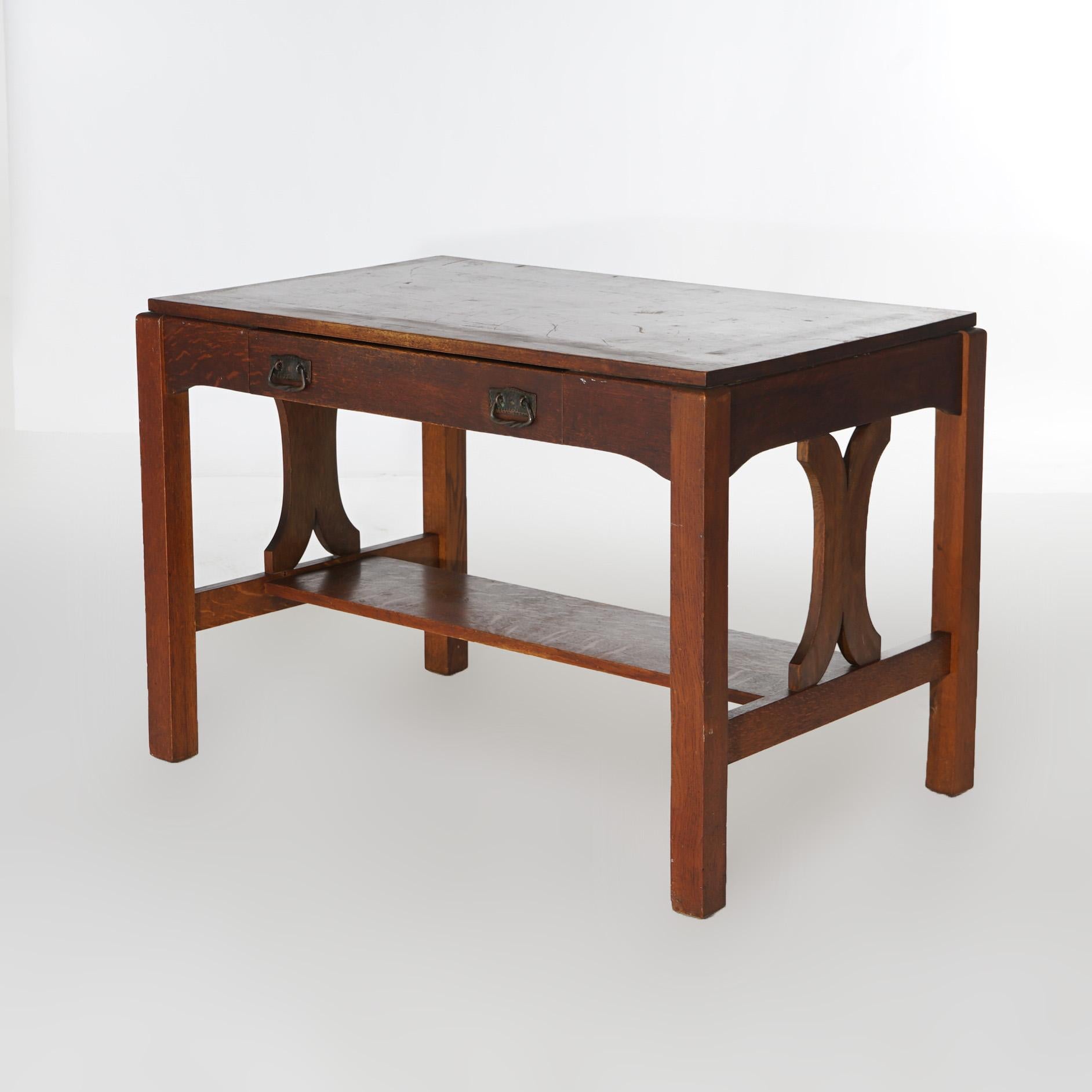 An antique Arts and Crafts Mission library table in the manner of Stickley offers quarter sawn oak construction with two drawers raised on trestle legs with stylized slat sides and lower shelf, c1910

Measures - 29.5