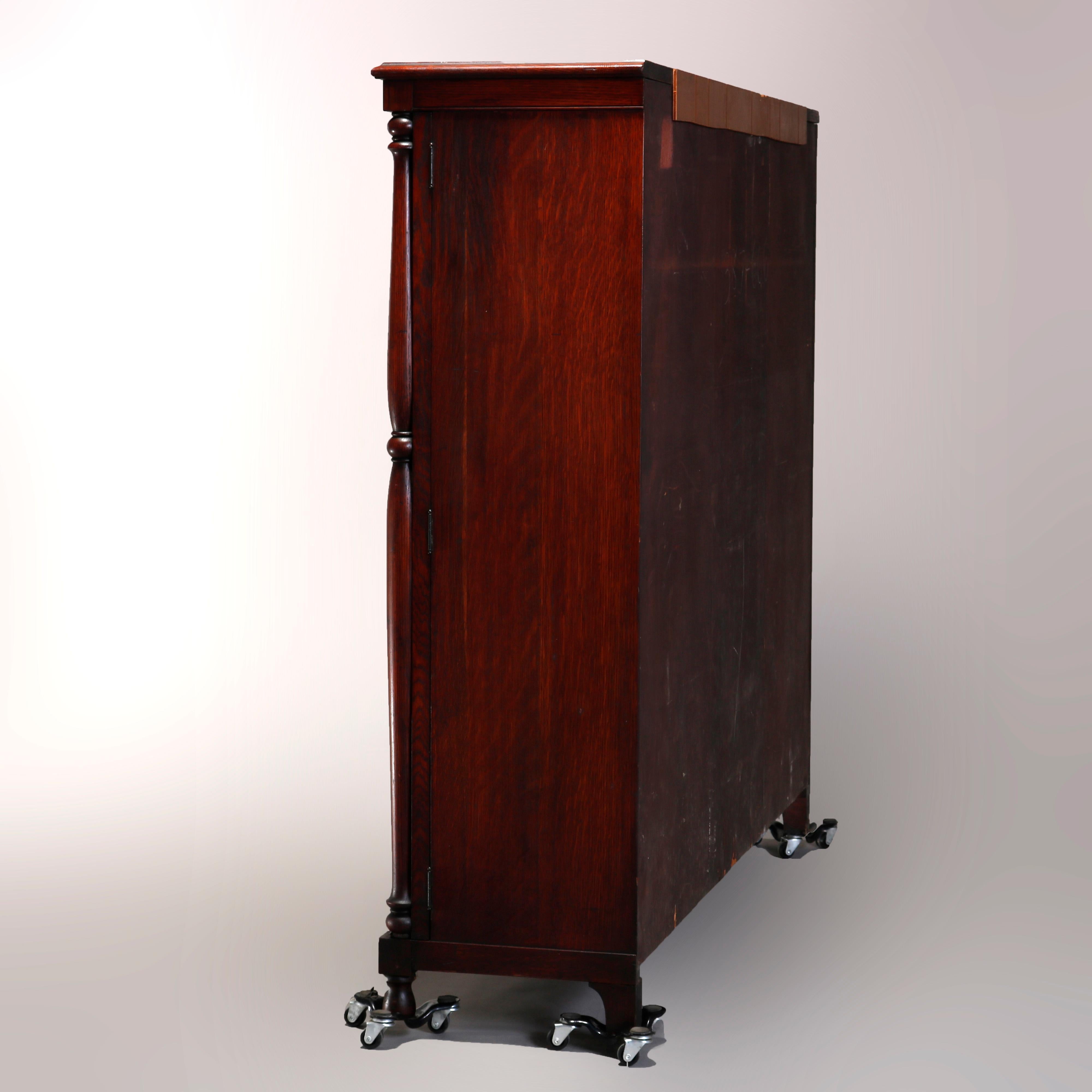An antique Arts & Crafts mission style bookcase offers oak construction with three glass doors opening to shelved interior, flanked by Doric style columns and raised on turned feet, circa 1910

Measures: 54.5