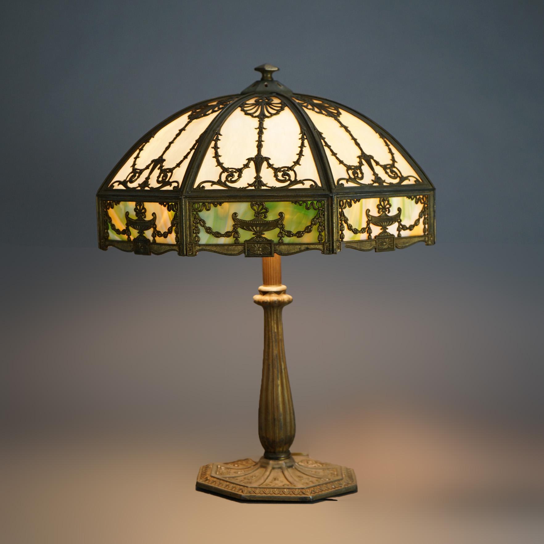 An antique Arts & Crafts table lamp by Bradley & Hubbard offers dome form shade with cast frame having Neoclassical urn and foliate design, housing two tone slag glass over a triple socket base, c1920

Measures- 23''H x 16''W x 16''D