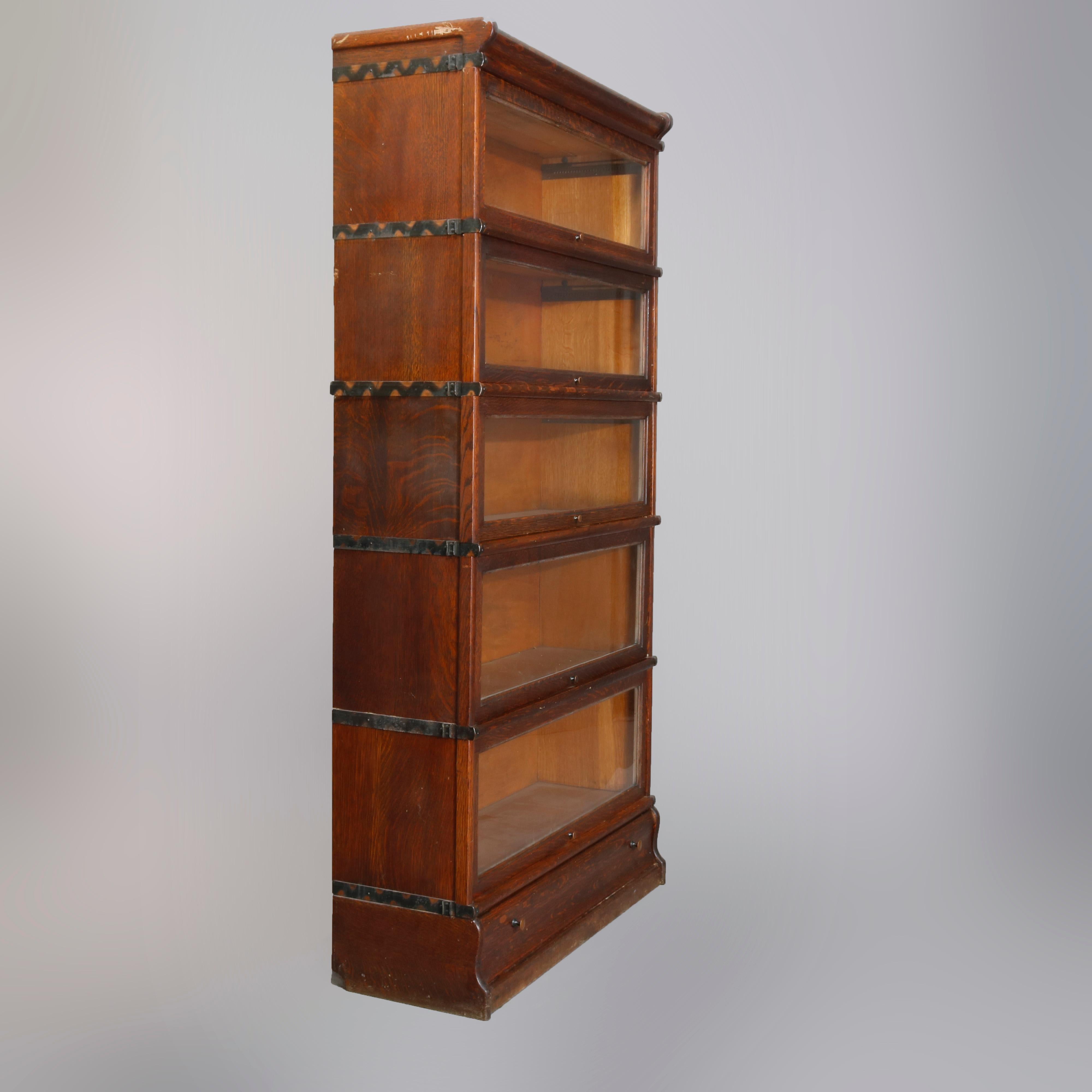 An Arts & Crafts sectional barrister bookcase by Macey, offers quarter sawn oak construction with five stacks each having a pull-down glass door on shaped base with drawer and surmounted by removable crown, maker stamped inside, circa