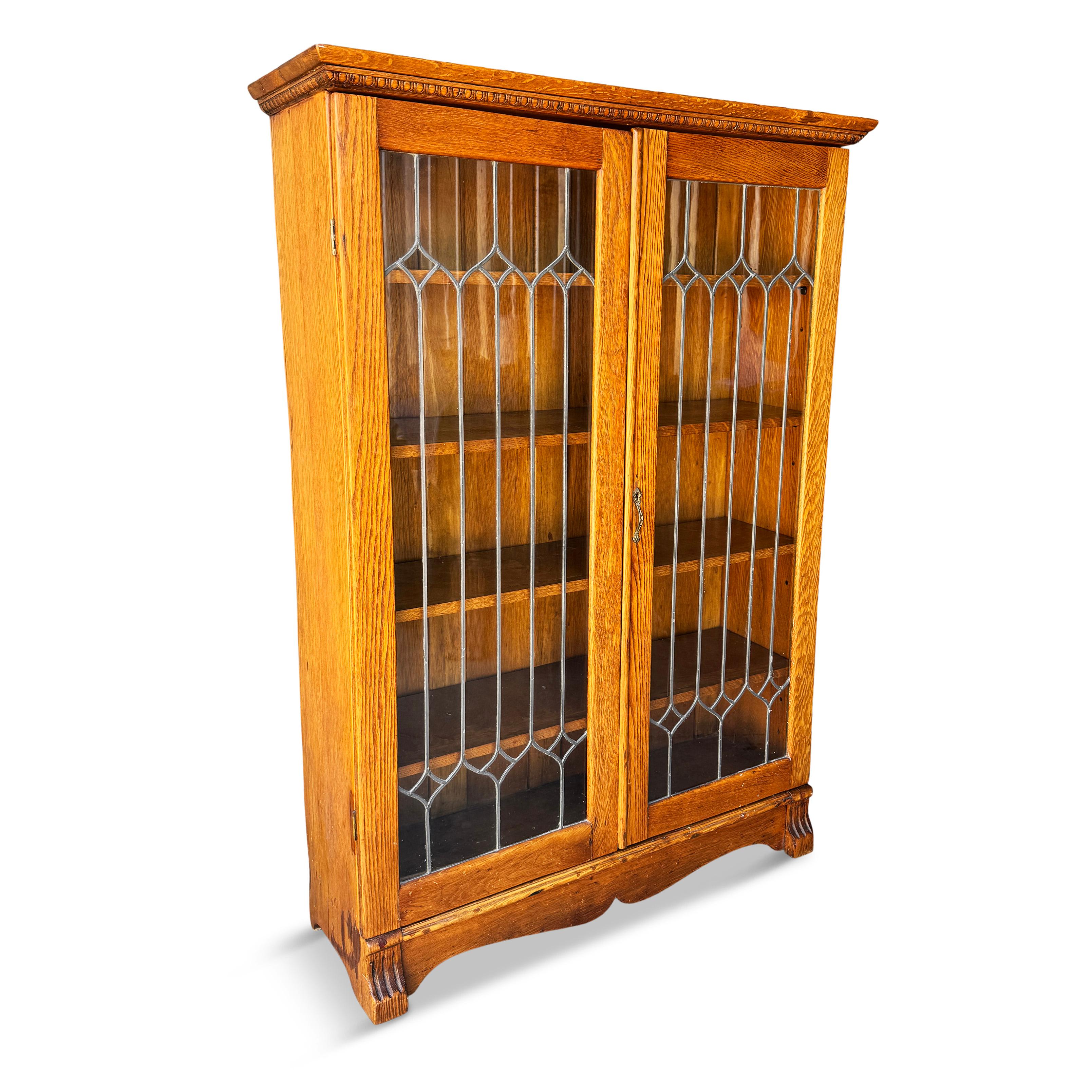 Showcase your treasured books and collectibles with this distinctive and beautiful antique Arts & Crafts oak bookcase.  With a design enhanced by leaded glass doors, hand carved feet and detailing, and four adjustable shelves, this book case is