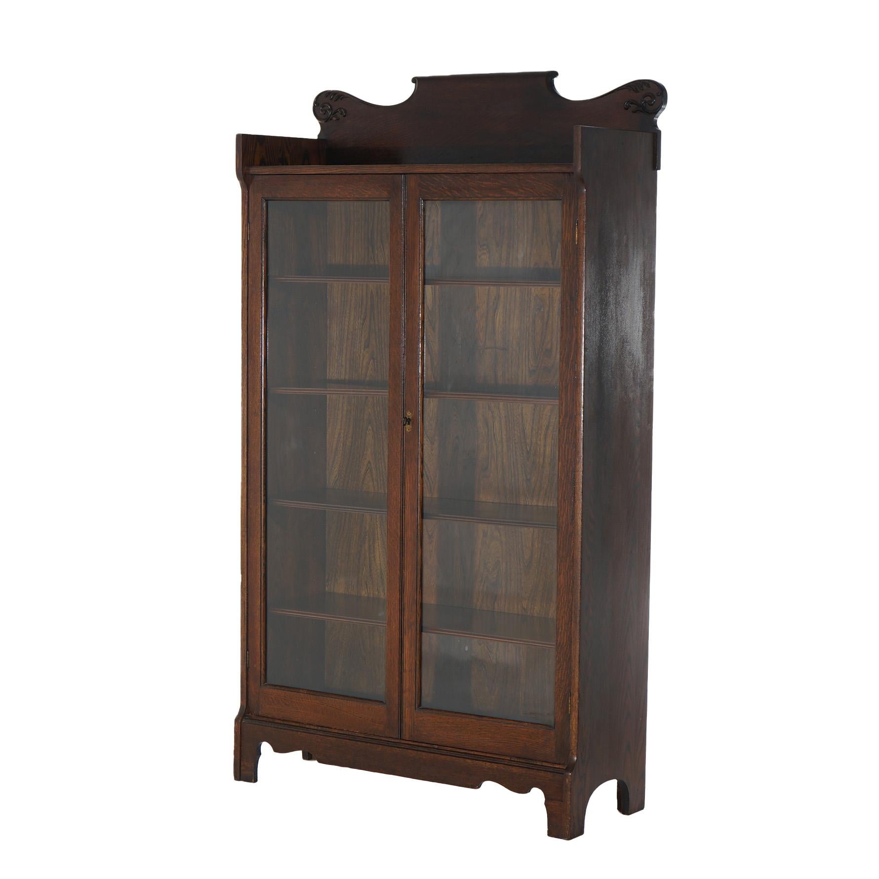 An antique Arts and Crafts bookcase offers oak construction with shaped crest over case having double glass doors opening to shelved interior, raised on stylized bracket feet, c1910

Measures - 64