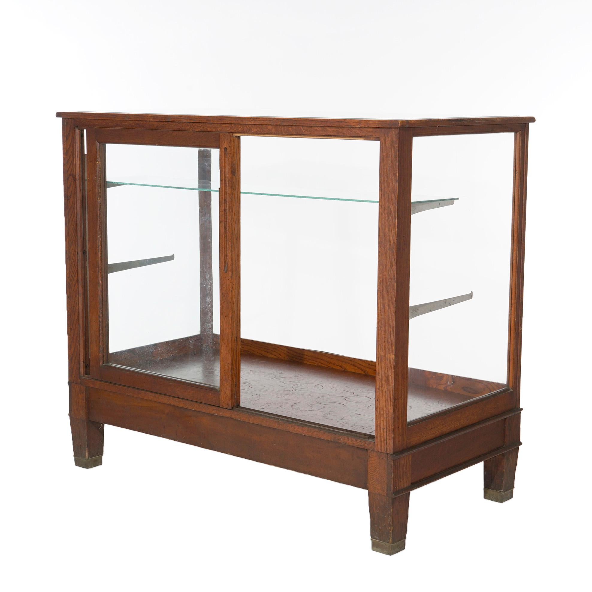An antique Arts and Crafts country store counter display case offers oak frame with sliding doors opening to adjustable shelf interior, raise on square and tapered legs, c1900.

Measures- 40.25''H x 47.25''W x 24''D.