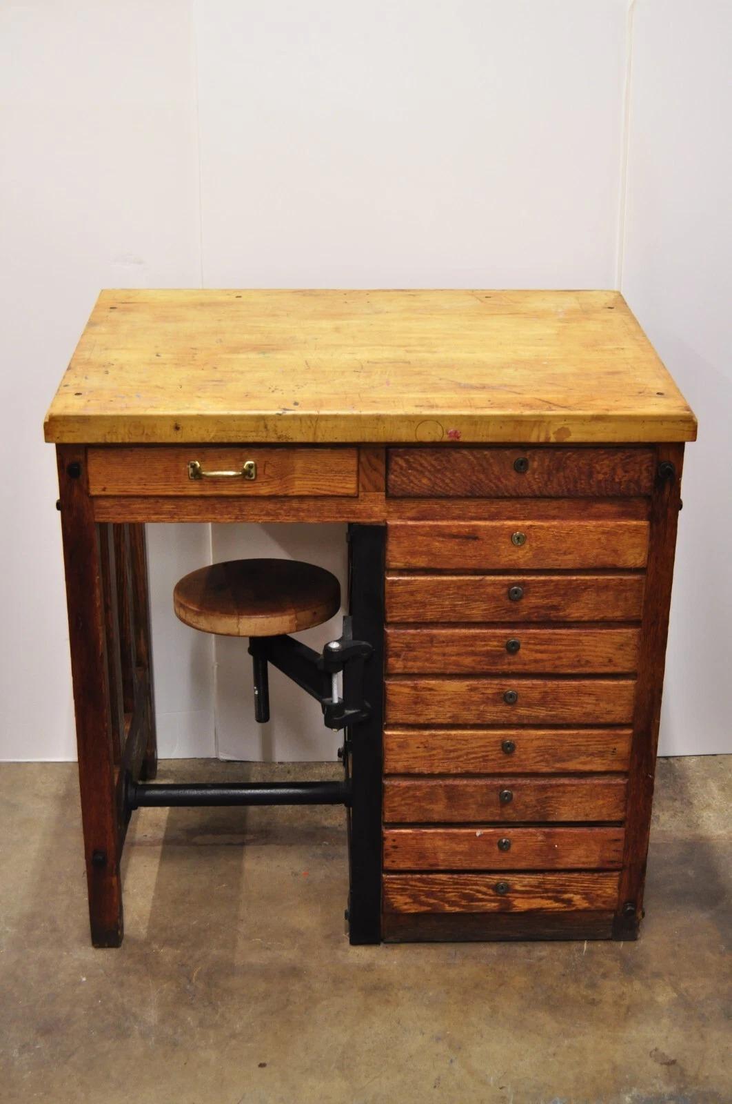 Antique English Arts & Crafts Oak Wood Watchmaker Jewelers Workbench. Item features a built in swivel/adjustable height stool with cast iron hardware, 10 drawers (writing to interior of drawers, a couple curse words), slanted top work surface, and