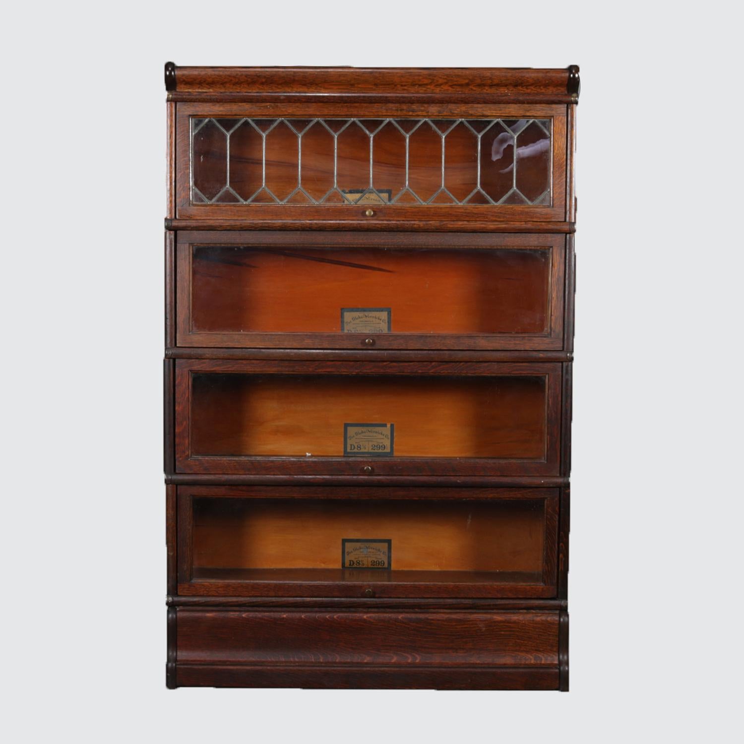 Antique Arts & Crafts barrister bookcase by Globe-Wernicke Co. features oak construction with crown over four stacked glass front cases, one with leaded glass, and base, original maker labels in each case, circa 1910.

Measures: 52.5