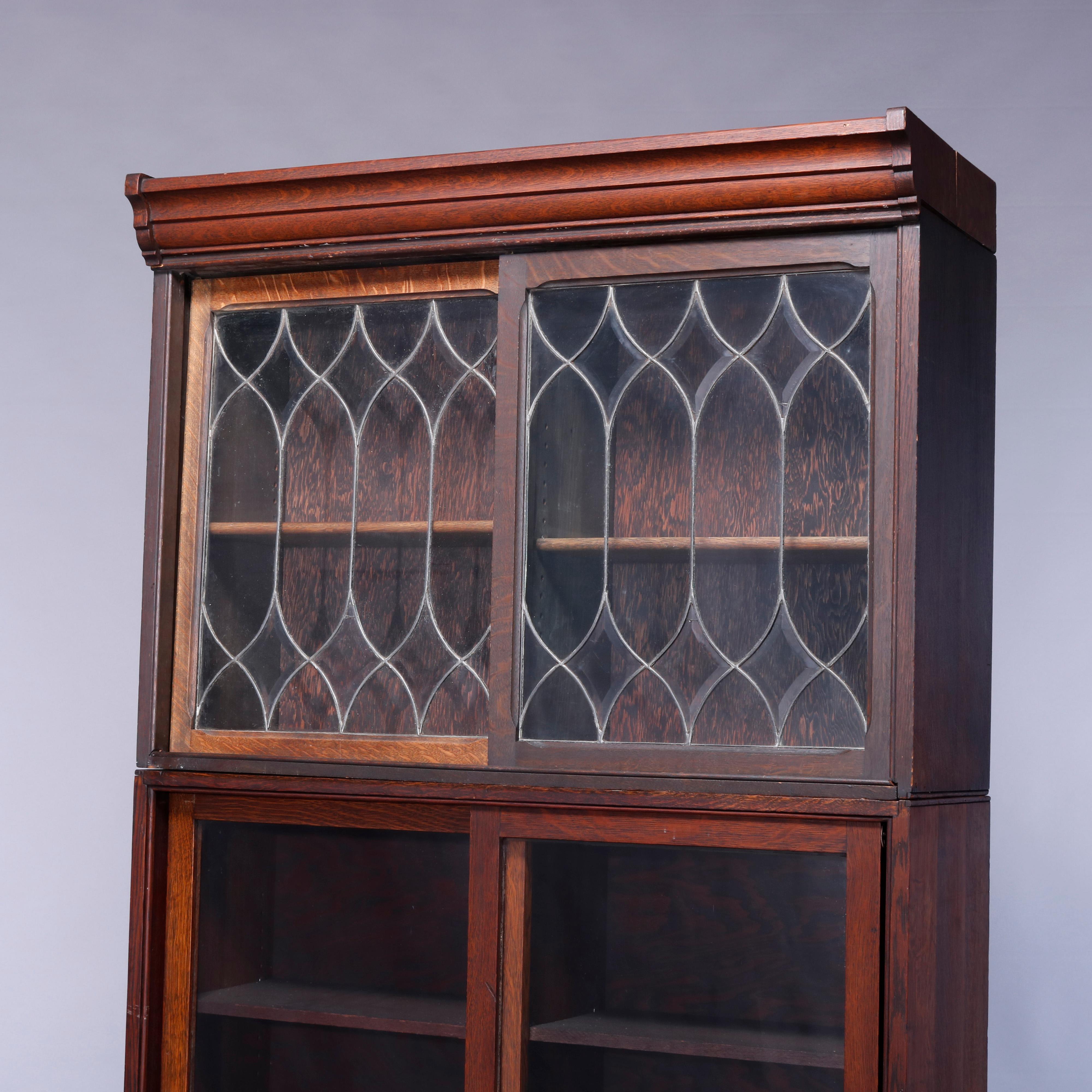 An Arts & Crafts antique Barrister bookcase offers oak construction with three sections, each having sliding glass doors opening to shelved interiors, the upper with leaded glass doors, raised on an ogee base, c1910

Measures: 82