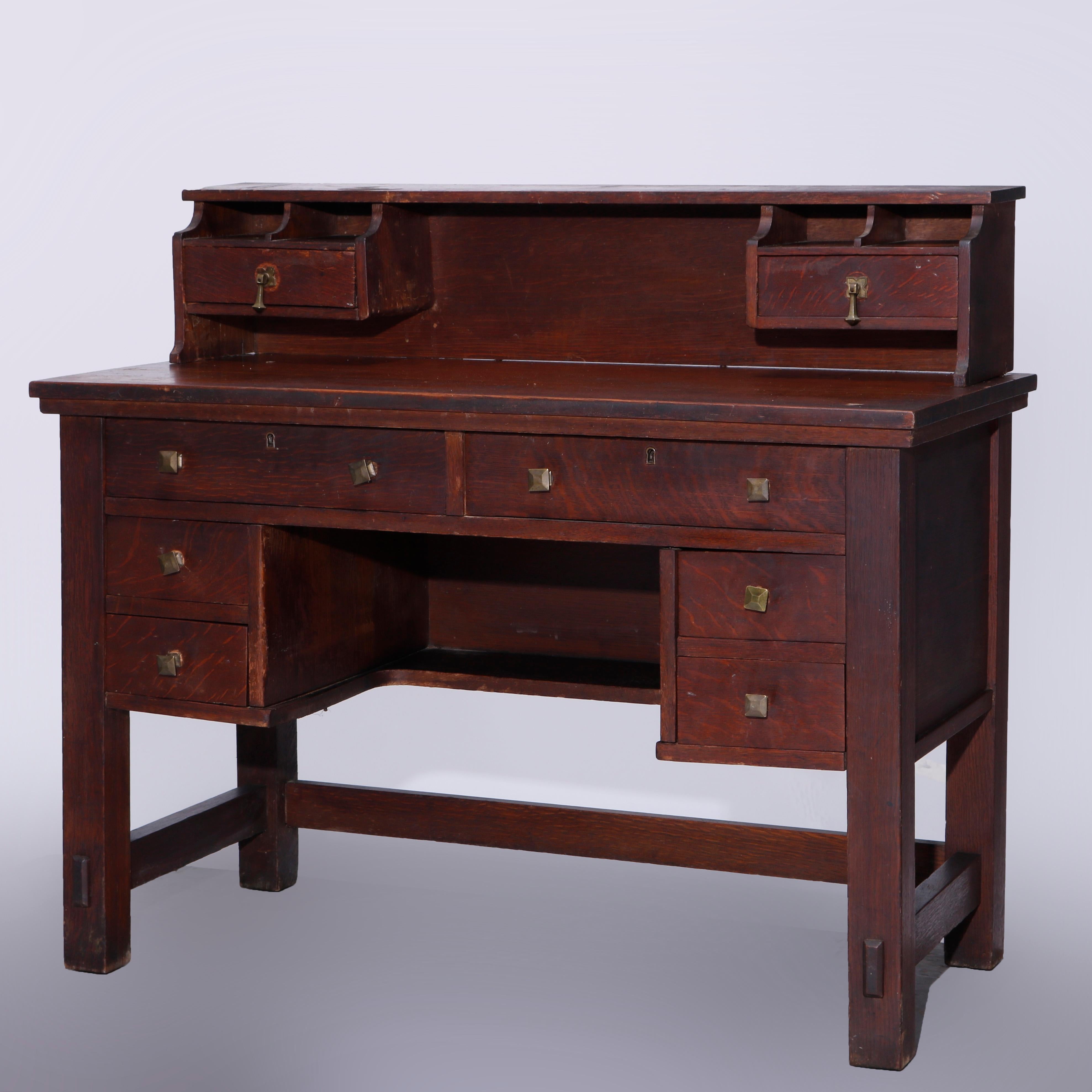 An antique Arts & Crafts postmaster desk offers oak construction in kneehole form with upper having storage drawers and pigeon holes over desk with central drawer and flanking drawer towers, raised on square and straight legs, c1900

Measures -