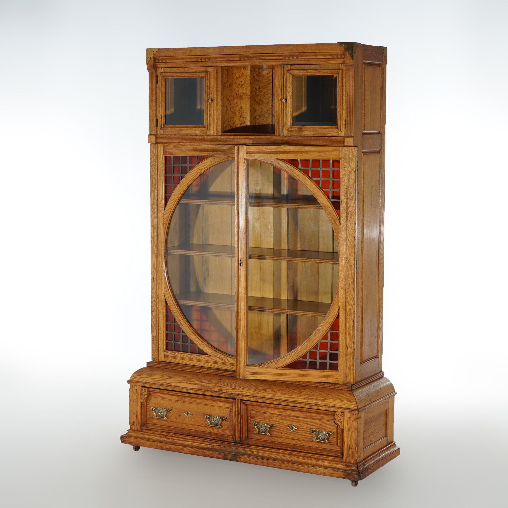 An antique Arts and Crafts bookcase offers oak paneled construction with case having upper double door cabinet over primary case with double glass doors having large central circular viewing element with leaded stained glass corbels and opening to