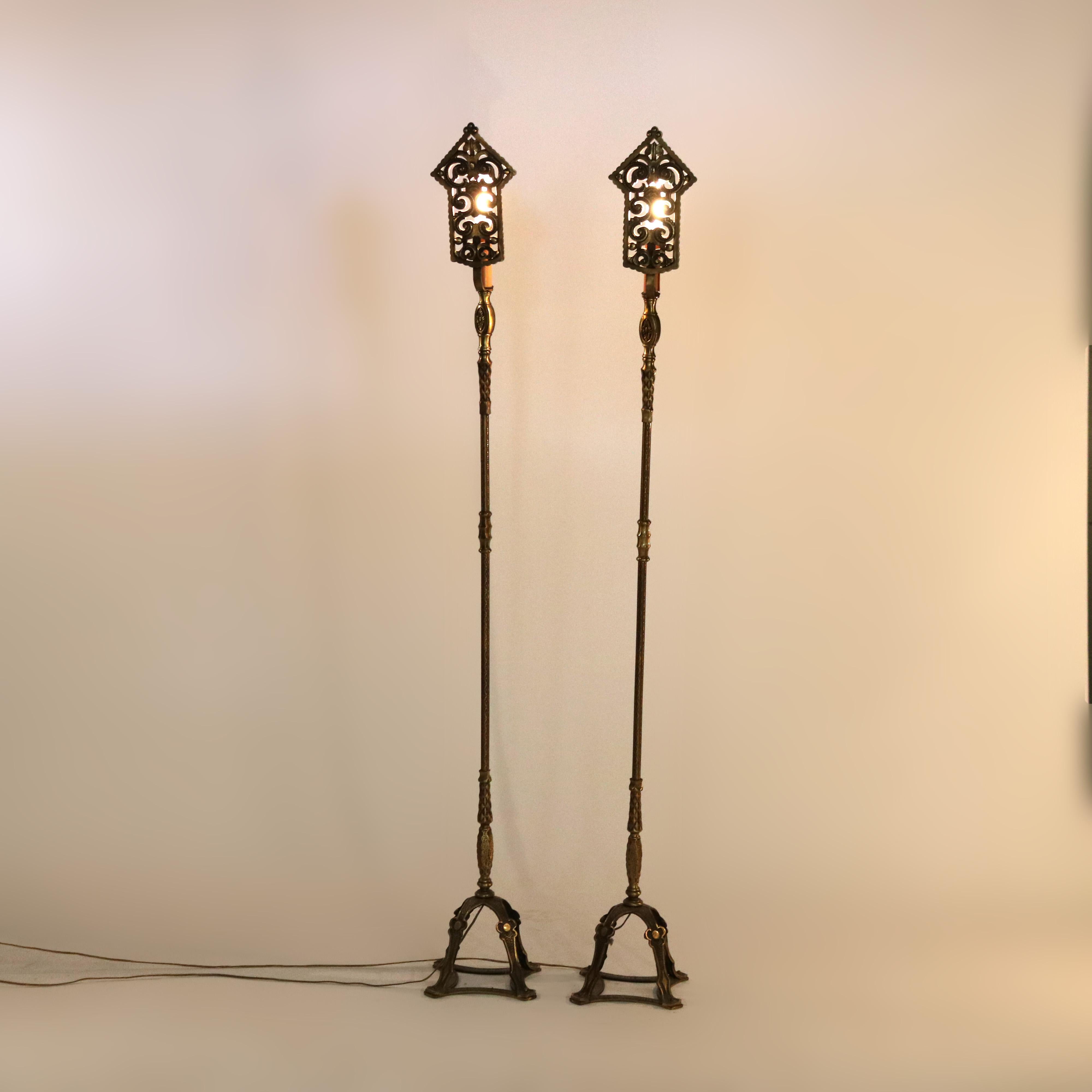 An antique pair of Arts and Crafts floor lamps attributed to Oscar Bach offer bronzed and gilt cast metal construction with upper pierced scroll panel screening candle light, raised on decorated column having four cabriole legs on framed base,