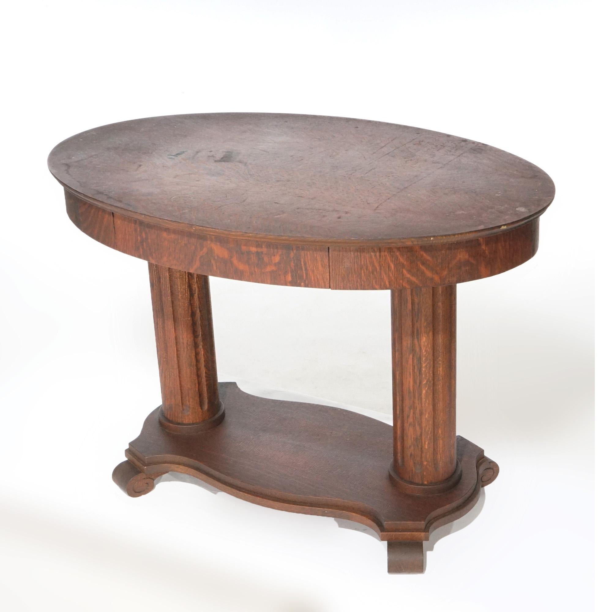 An antique Arts and Crafts library table offers quarter sawn oak construction with top in oval form over straight skirt with single drawer, raised on double reeded column base, c1910

Measures- 29''H x 41.75''W x 26''D.