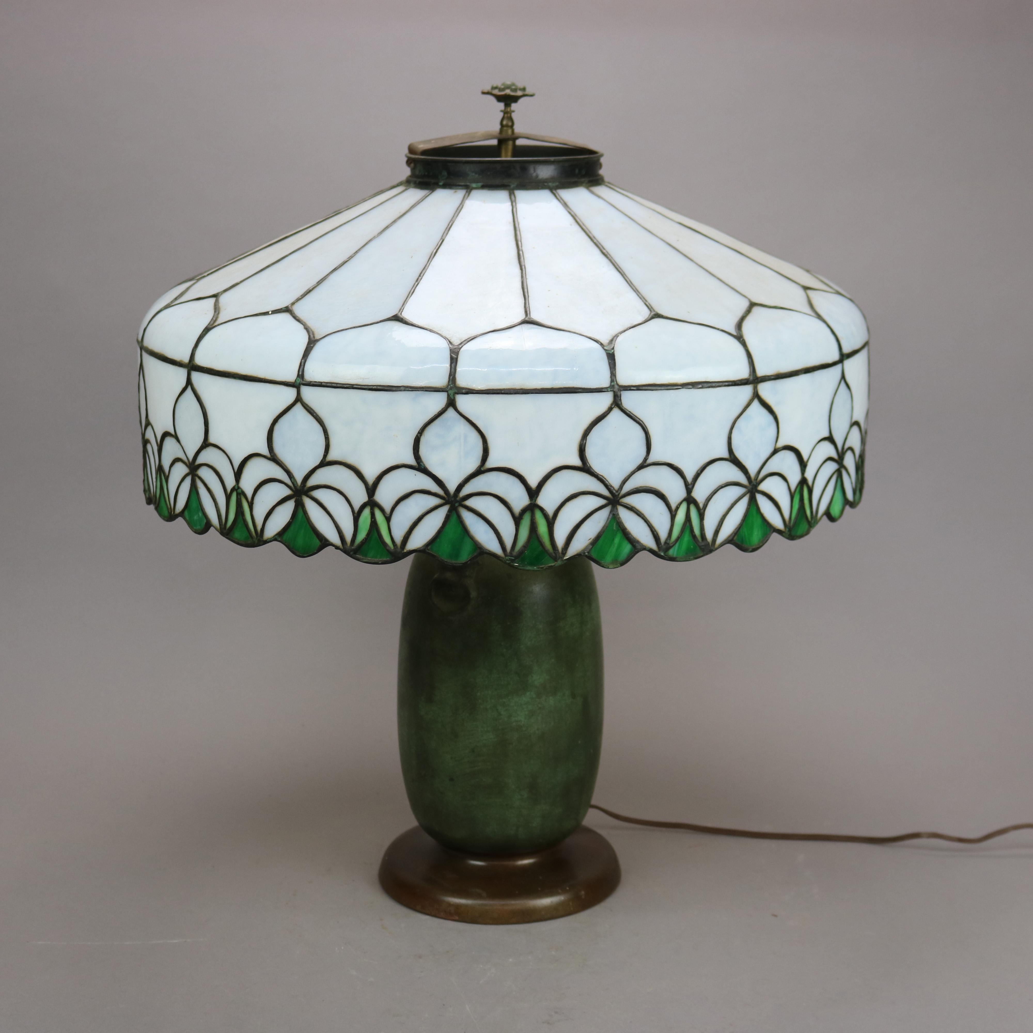 An antique large Arts & Crafts table lamp by Charles Parker offers leaded glass shade having floral bordering surmounting figural green metal double socket base with flanking lion handles, maker label on base as photographed, c1920

Measures -