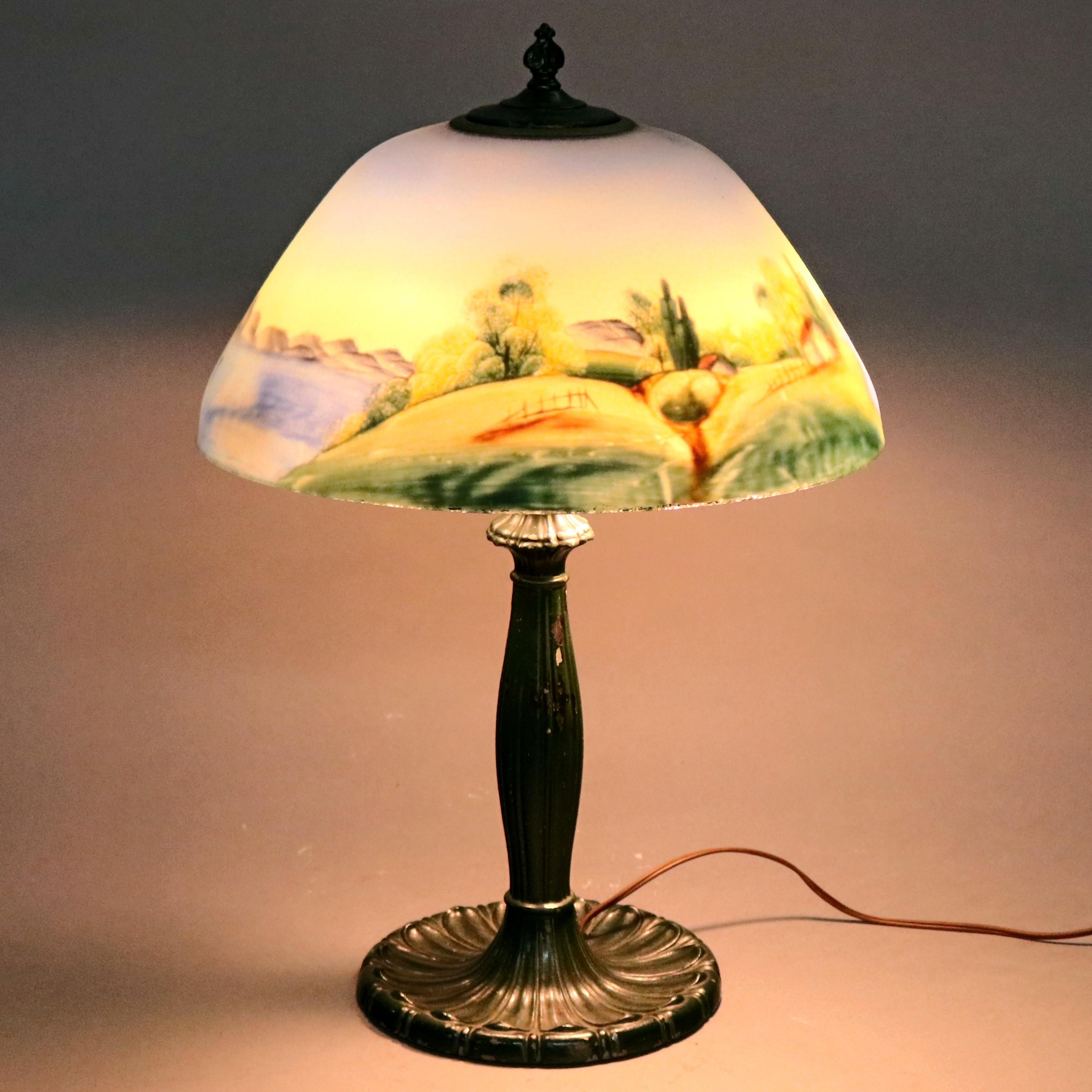 An antique Arts and Crafts Pairpoint School table lamp offers reverse painted glass shade with landscape scene having cottage in countryside setting, raised on cast base with independently controlled double sockets, c1920

Measures - 17.5