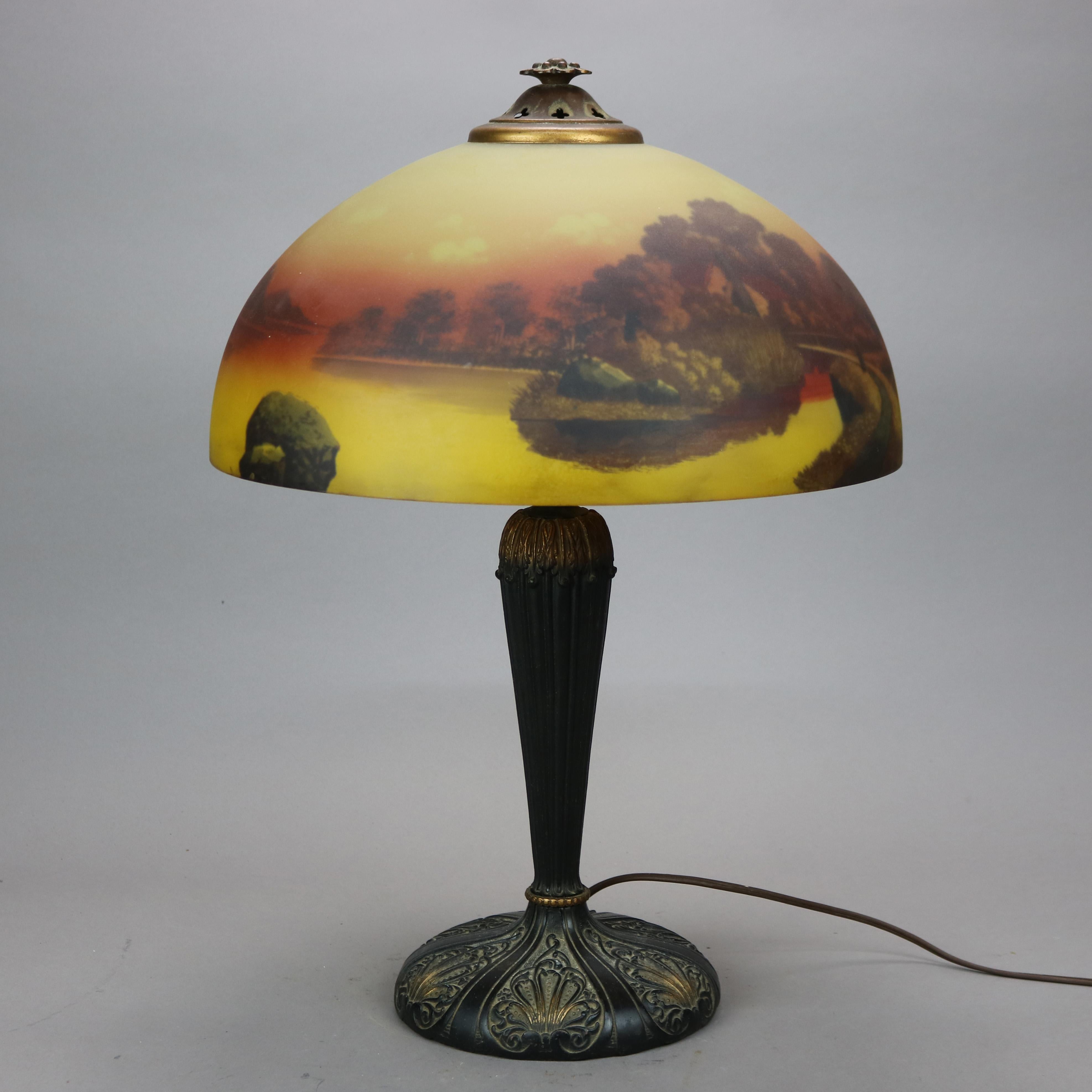 An antique Arts & Crafts table lamp by Phoenix offers reverse painted dome glass shade with landscape lake scene over double socket base having scroll and foliate embossed elements, c1920.

Measures- 22''H x 16''W x 16''D.