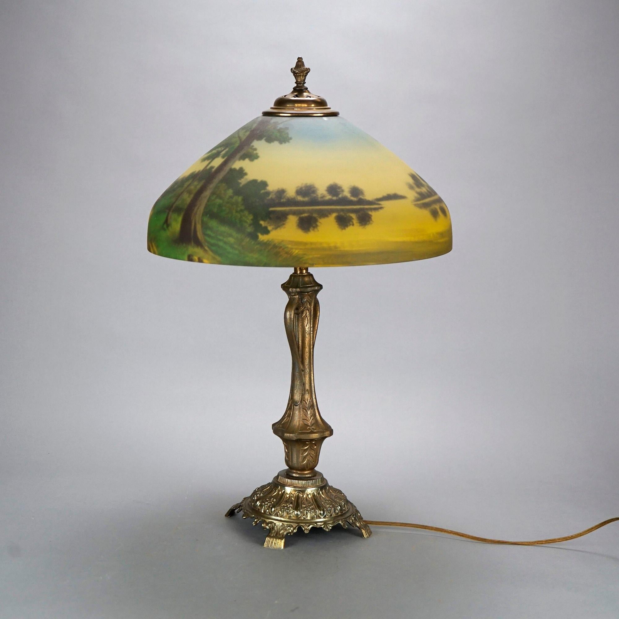 An antique Arts and Crafts Phoenix table lamp offers dome form glass shade with reverse painted lake scene over double socket cast base raised on foliate embossed footed plinth, c1920.

Measures- 25''H x 16''W x 16''D.

Catalogue Note: Ask about