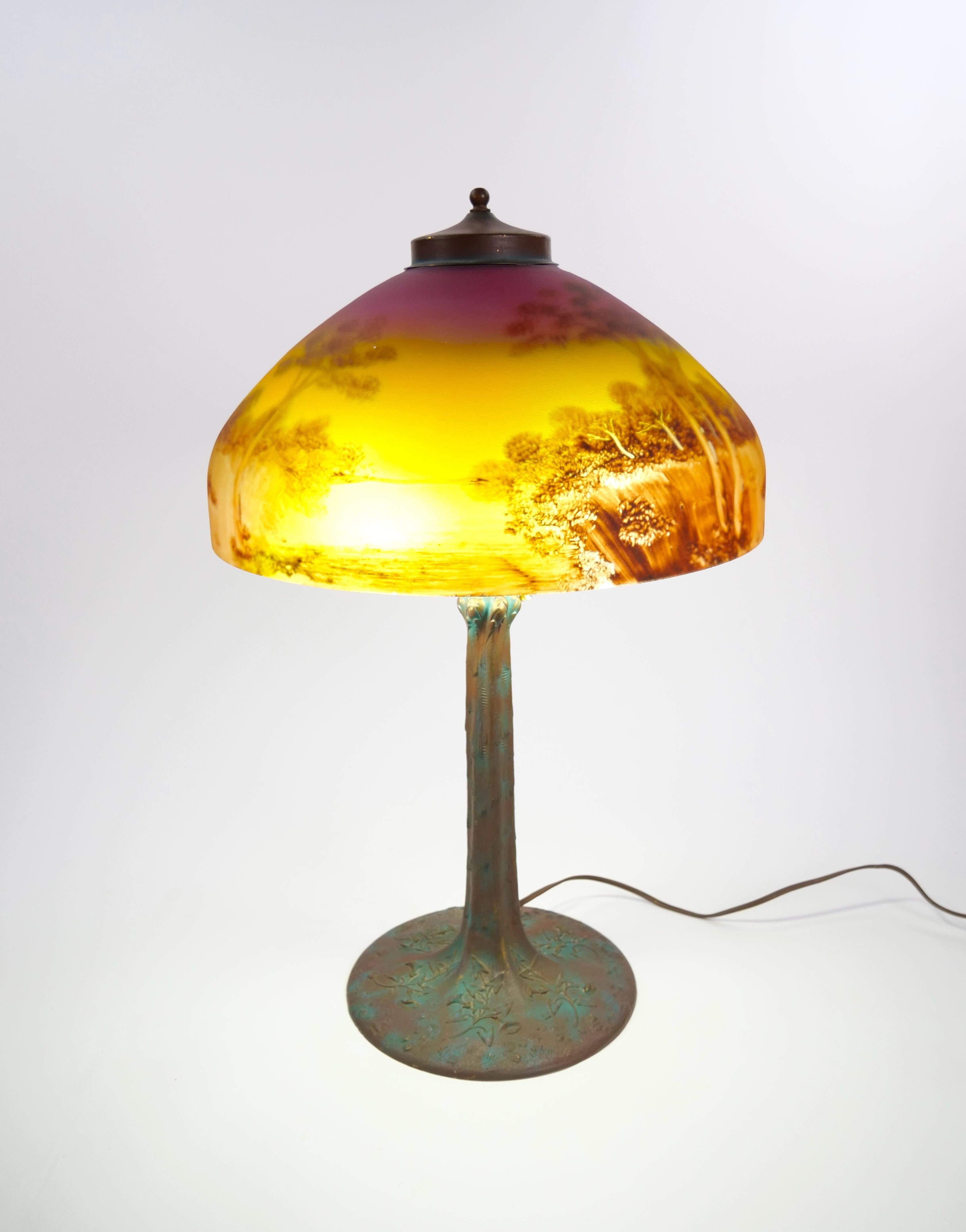 Exemple captivant de l'éclairage américain du début du XXe siècle, cette lampe de table antique de l'Arte Antiques & Crafts, attribuée à Phoenix, présente un abat-jour en dôme de verre peint à l'envers richement détaillé, représentant un paysage
