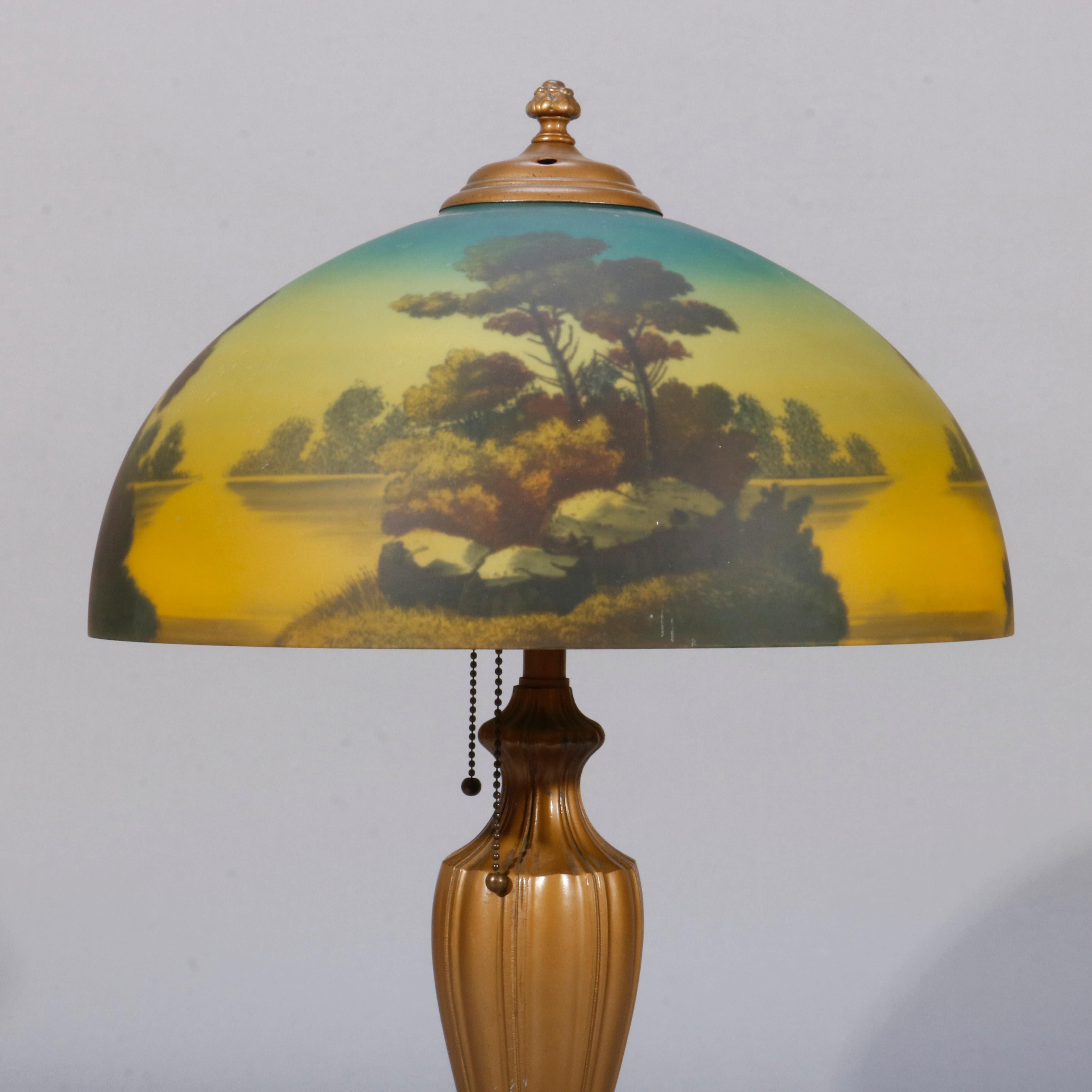 An antique Arts & Crafts Phoenix table lamp offers reverse painted domed shade with landscape lake scene surmounting double socket urn form base, circa 1920

Measures- 23