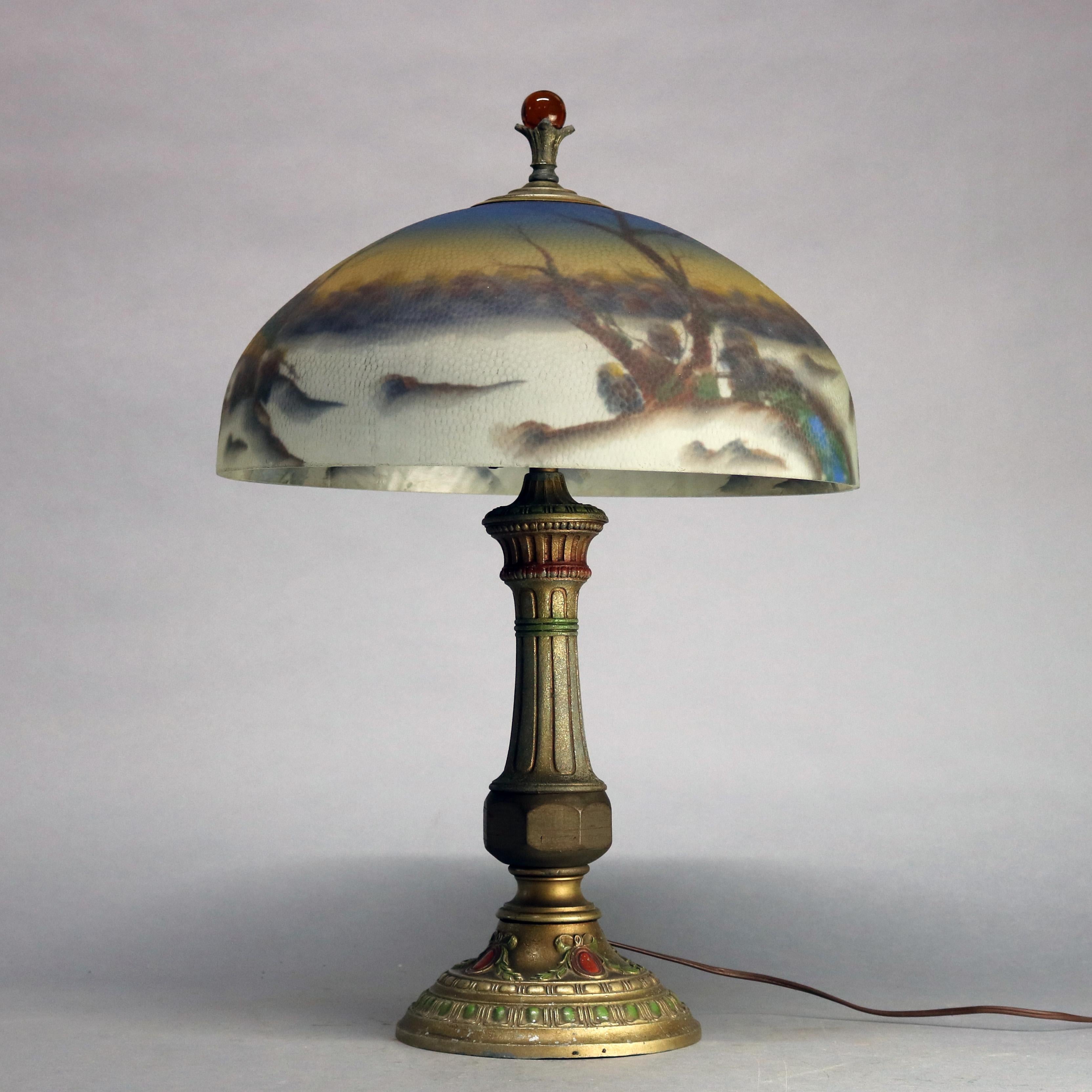 An antique Arts & Crafts table lamp in the manner of Pittsburgh offers reverse painted glass dome shade with winter landscape scene having structure surmounting polychromed cast double socket base with jeweled finial, circa 1920

Measures: 24.5