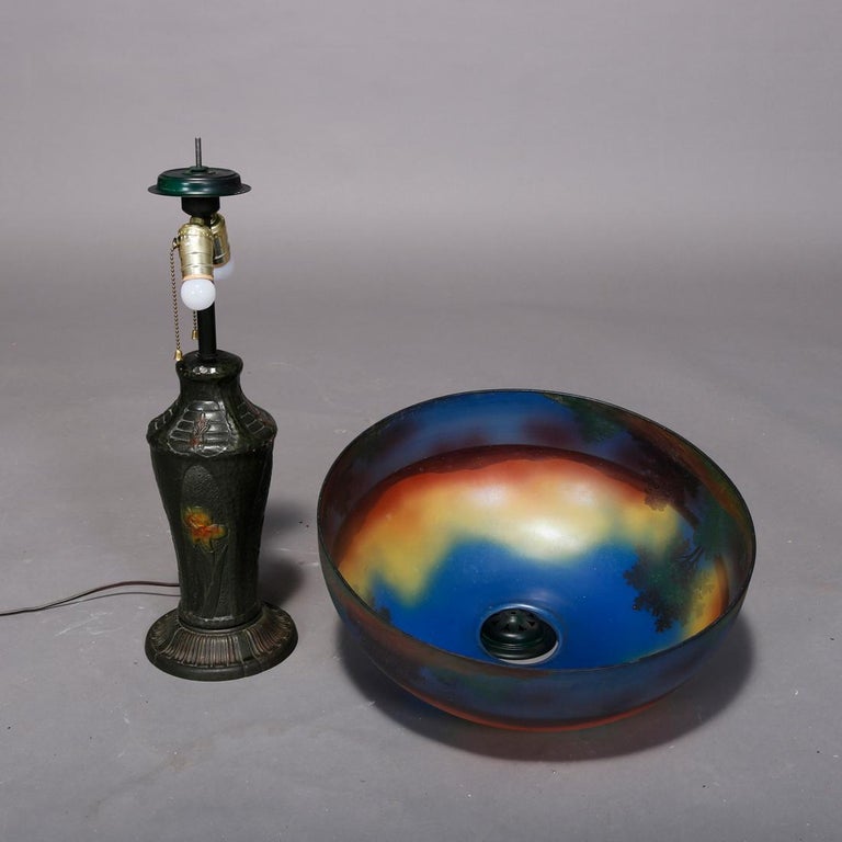 An antique Arts & Crafts table lamp in the manner of Pittsburgh ight Co. offers reverse painted dome shade with landscape scene surmounting case double socket base having reserves with polychromed flowers, c1920

Measures: 24