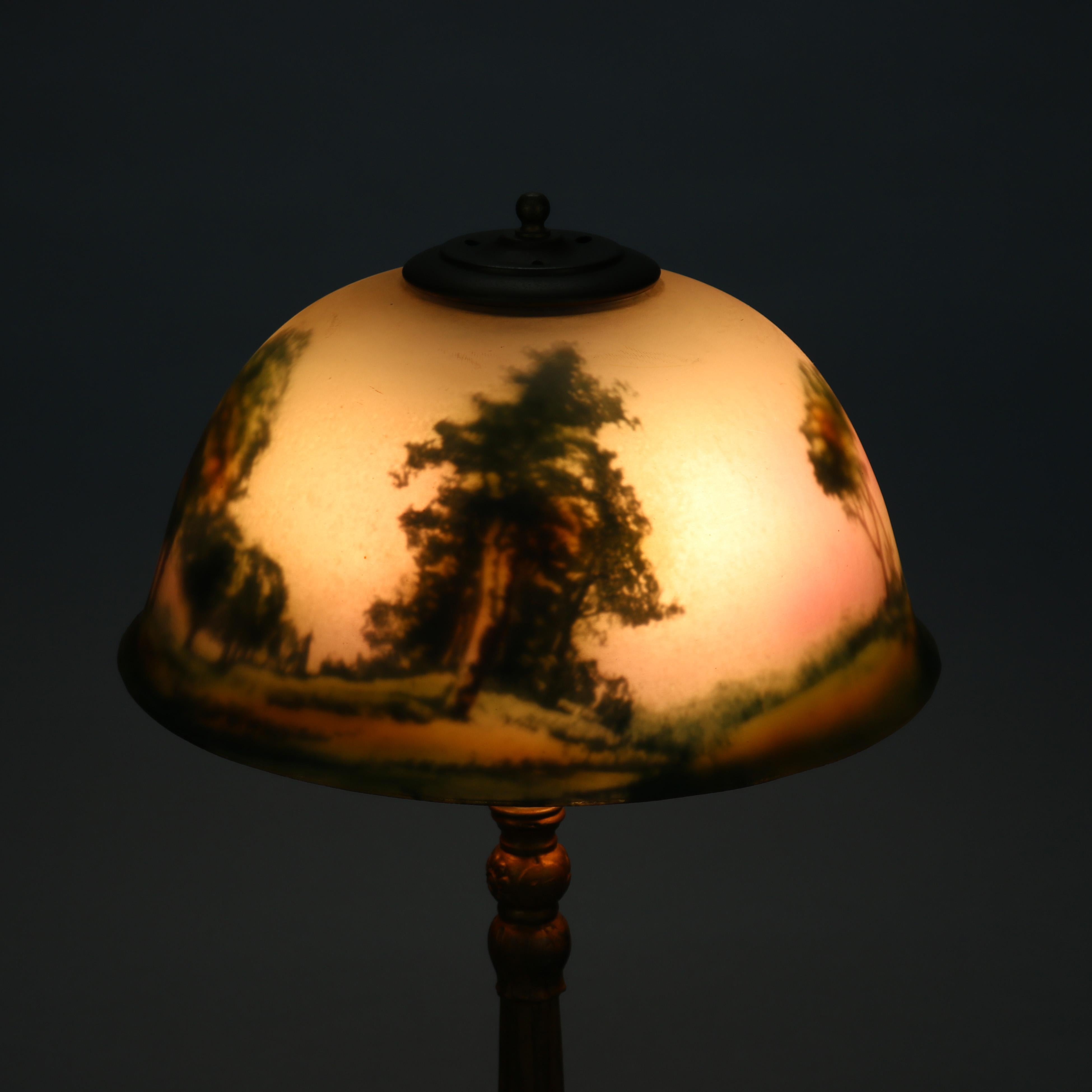 An antique Arts and Crafts table lamp offers reverse painted glass shade having landscape scene over cast double socket base, c1920

Measures: 19