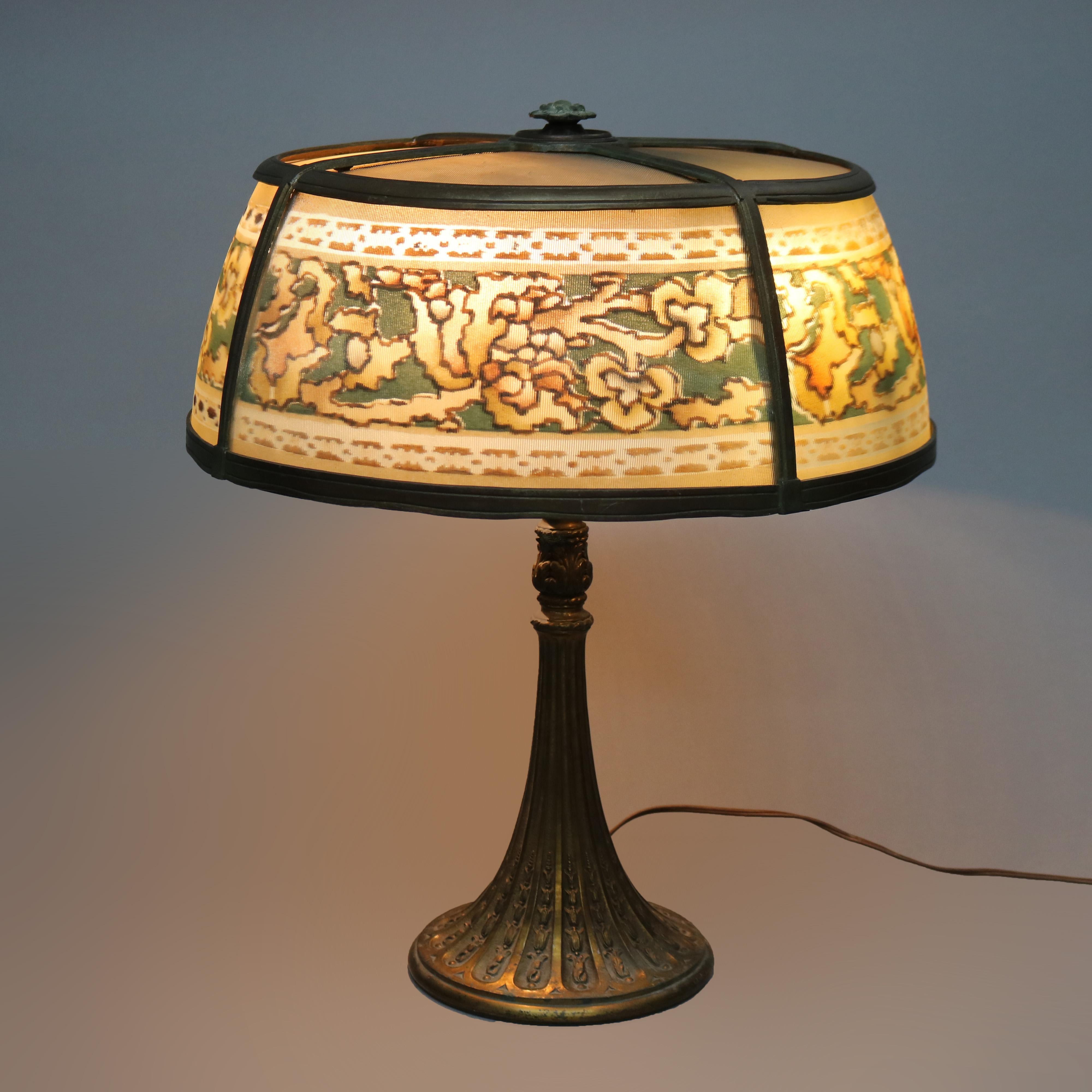 An antique Arts and Crafts table lamp in the manner of Bradley and Hubbard offers shade having stylized floral band surmounting double socket flared base with reeding with inverted bellflowers, c1920

Measures - 22.25''H x 18.5''W x 18.5''D.