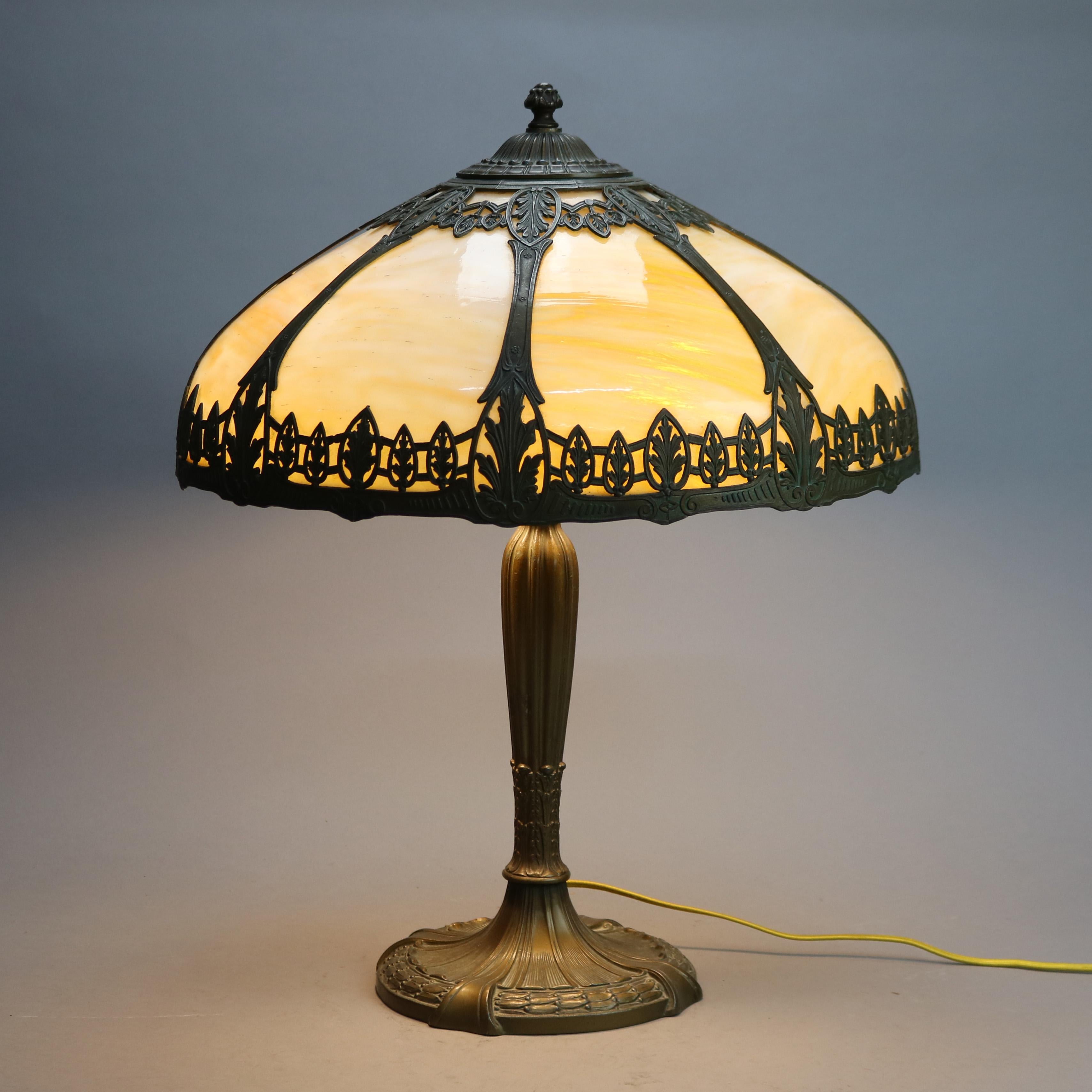 An antique Arts and Crafts table lamp by Royal Art Glass Co offers dome shade with cast filigree frame having stylized foliate elements and housing eight curved slag glass panels, over cast double socket base, maker mark on base as photographed,