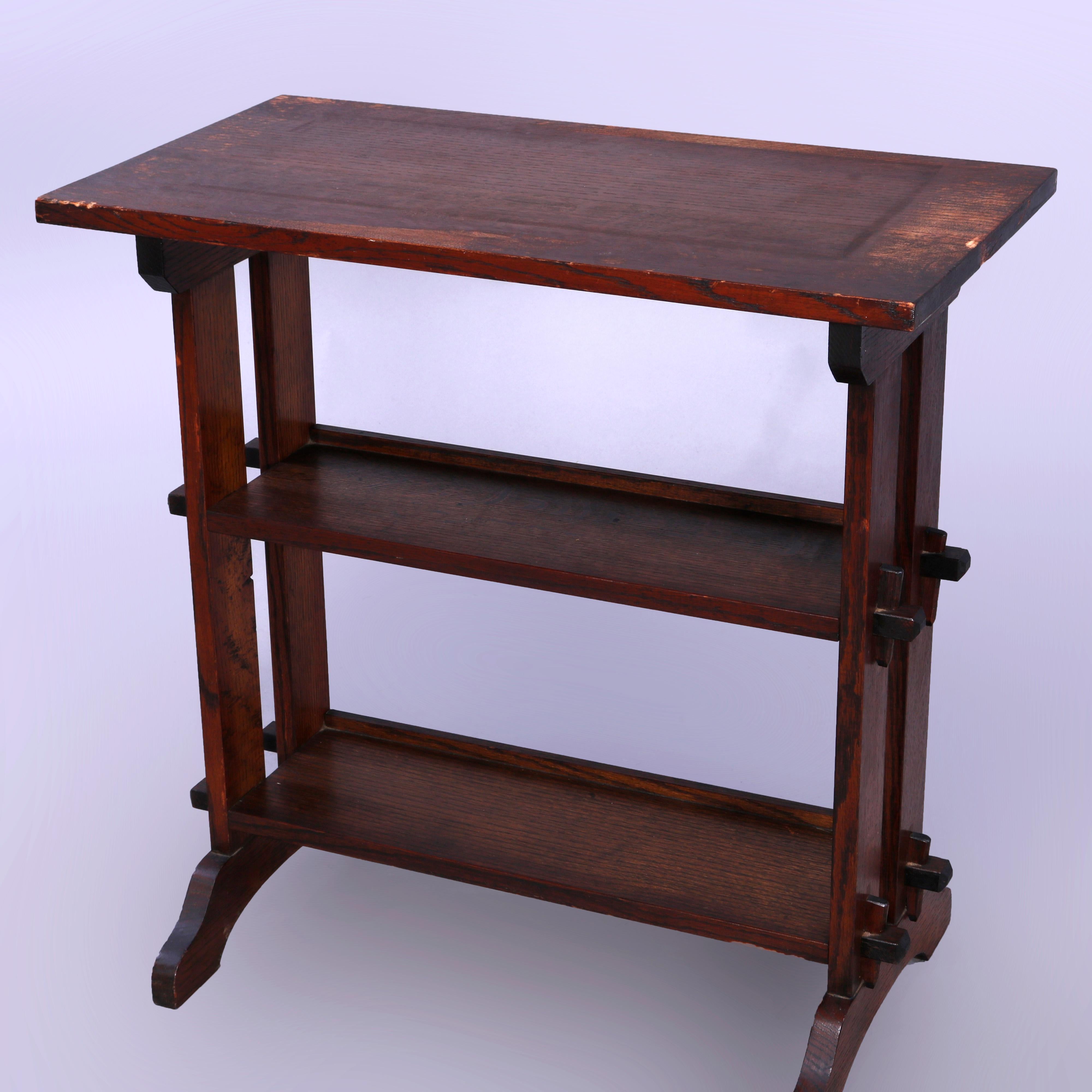 An antique Arts and Crafts Journey book stand by Roycroft offers oak mortise and tenon construction in trestle form with top shelf surmounting two lower book trays flanked by slat sides land raised on arced legs, maker label on base as photographed,