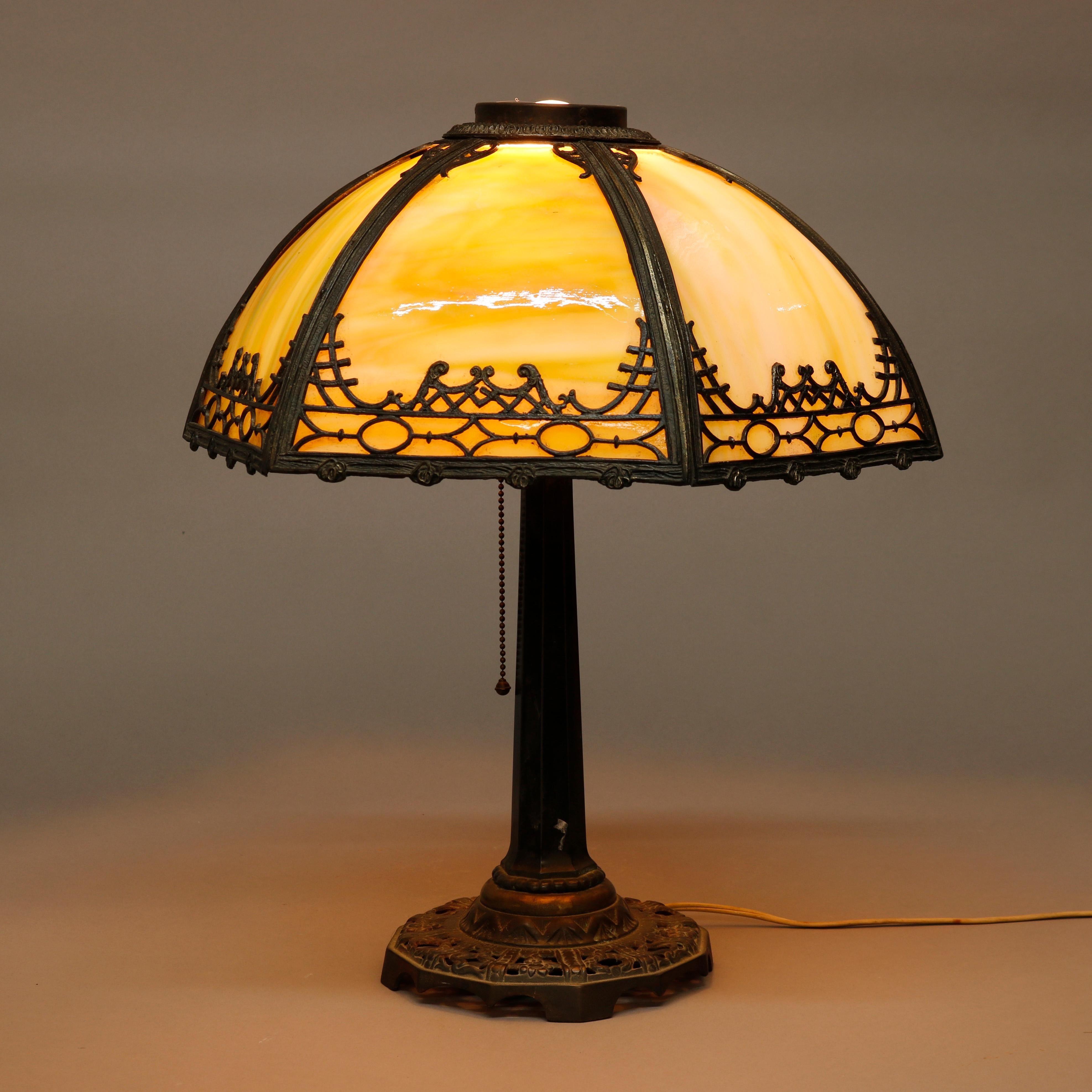 An antique Arts & Crafts table lamp by Bradley and Hubbard offers cast filigree shade housing bent slag glass panels and surmounting single socket base having faceted column on filigree foot, maker signed, c1920

Measures - 19'' H X 17'' W X 15''