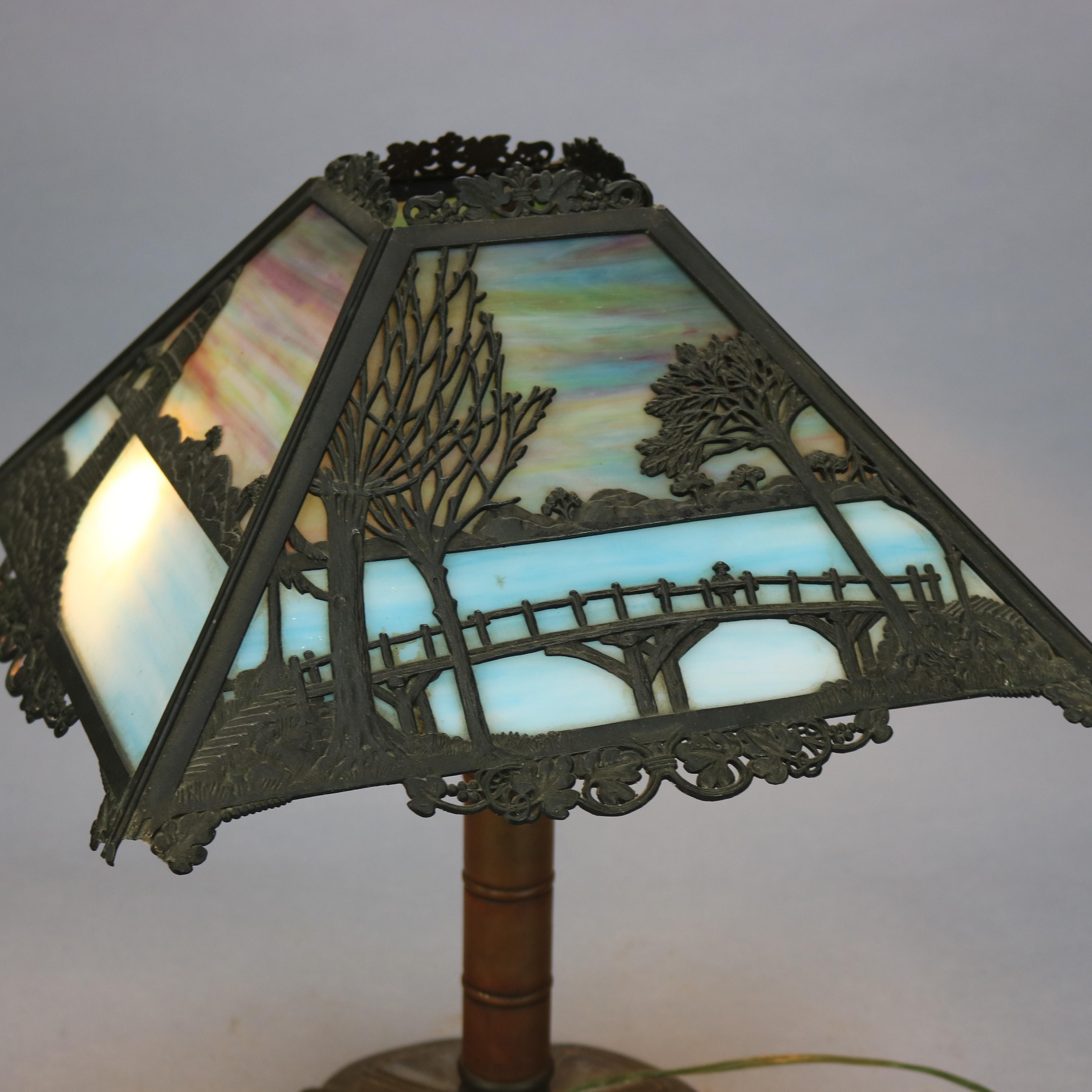 An antique Arts & Crafts scenic table lamp by Bradley and Hubbard offers cast scenic shade with pierced seaside scene with shoreline, lighthouse and bridge housing two toned slag glass over double socket base, signed B&H, c1920.

Measures: 18.5