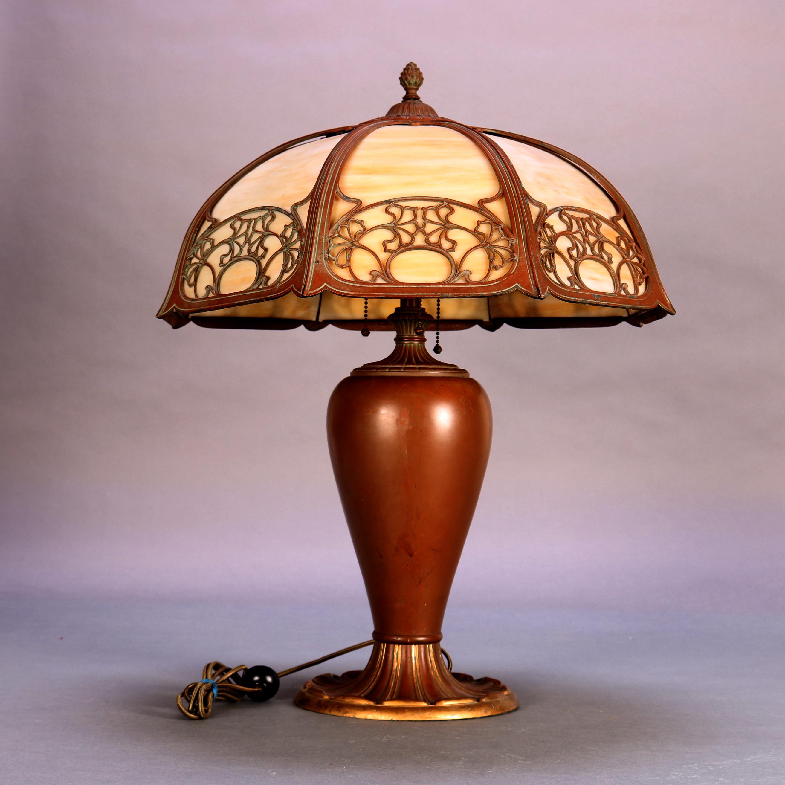 An antique Arts & Crafts table lamp by Bradley Hubbard offers cast 8-panel shade with stylized floral decoration housing bent slag glass and surmounting urn form triple socket base, circa 1920

Measures- 24.5