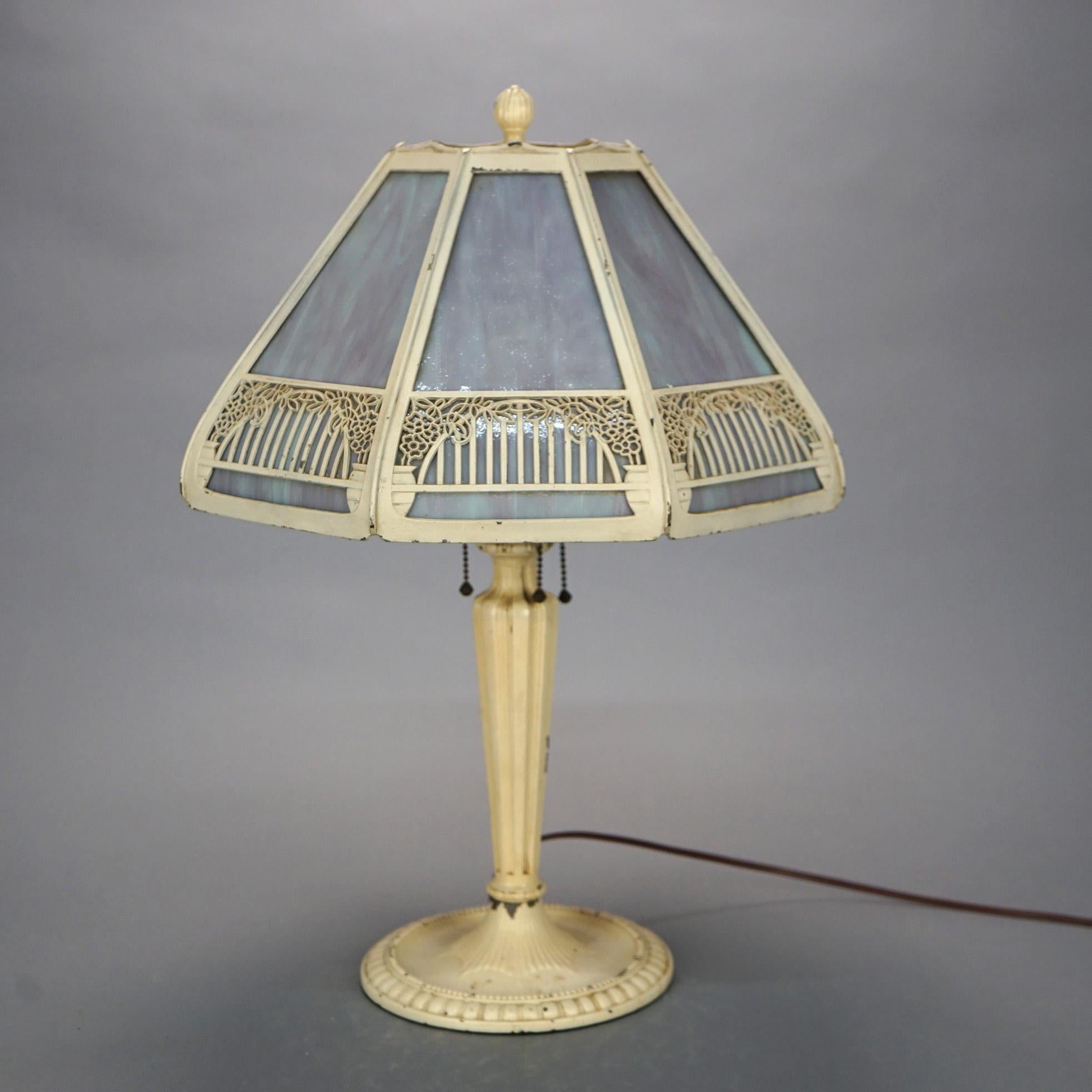 An antique Arts & Crafts table lamp offers cast shade with stylized floral filigree housing paneled slag glass over triple socket cast base, c 1920.

Measures: 22.5'' H x 15.5'' W x 15.5'' D.