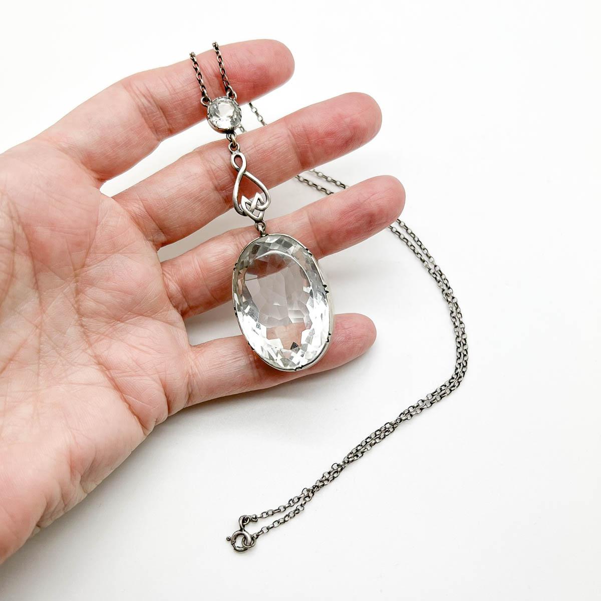 A divine antique rock crystal drop pendant from the 1900s. A huge piece of rock crystal with a large flat table and deep faceted pavilion is set in a deep band of sterling silver dropping from an Arts & Crafts design top finished with a smaller