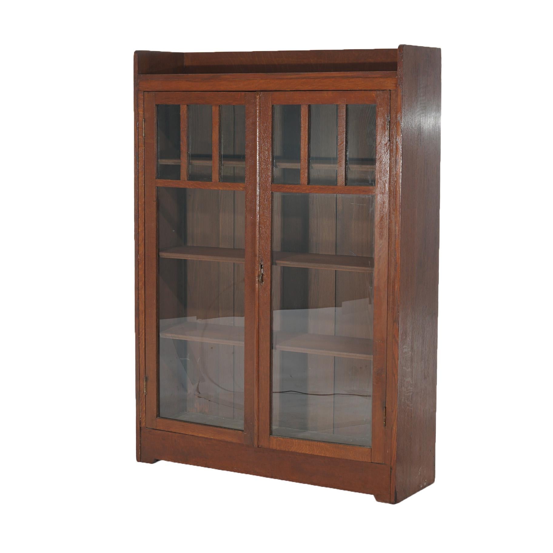 An antique Arts and Crafts Mission bookcase by Stickley offers oak construction with upper gallery surmounting lower case having double glass doors opening to shelved interior, circa 1910

Measures - 57.5