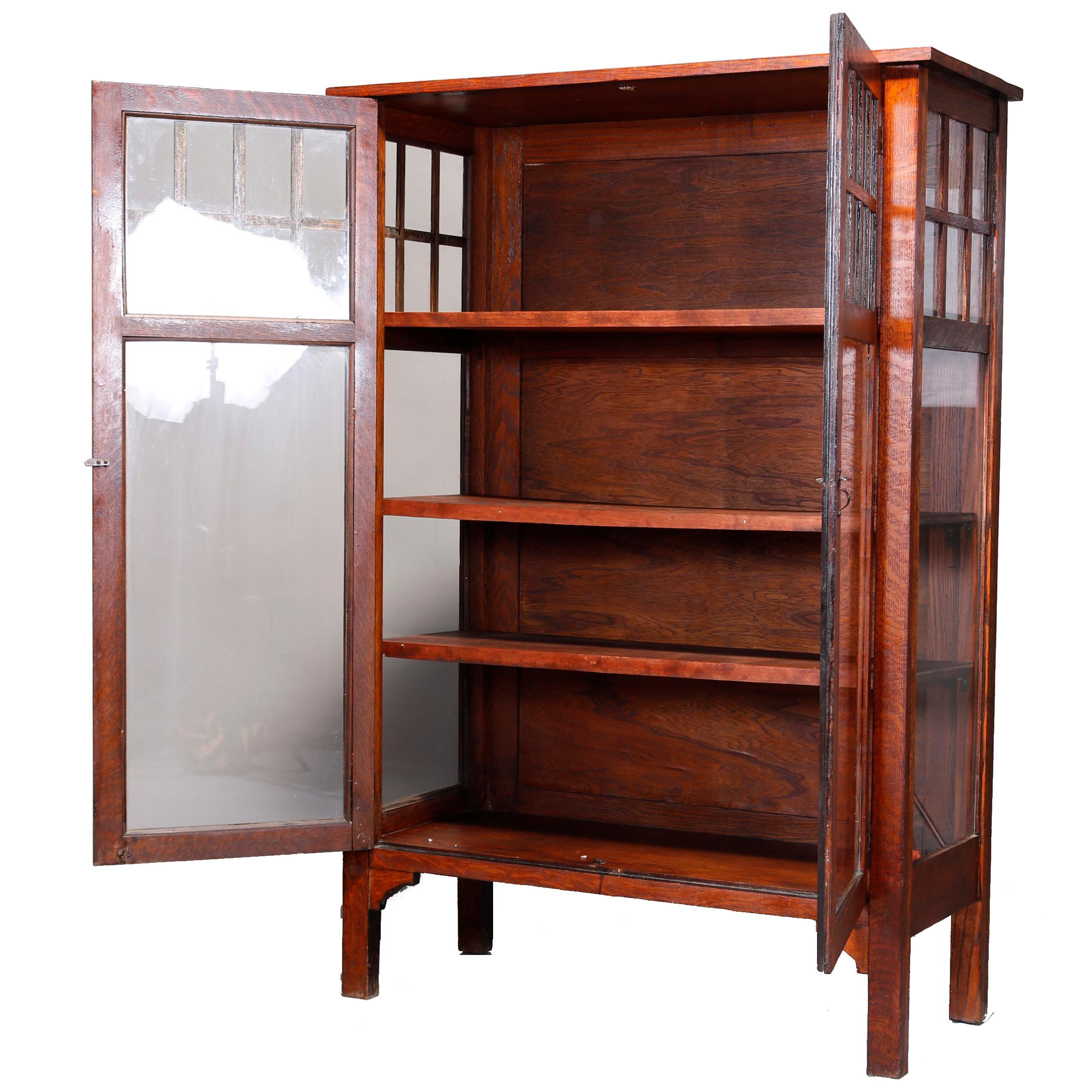 An antique Arts & Crafts Mission china cabinet in the manner of Stickley offers oak construction with double glass doors opening to shelved interior with upper quarter with mullioned styling, raised on straight and square legs, circa