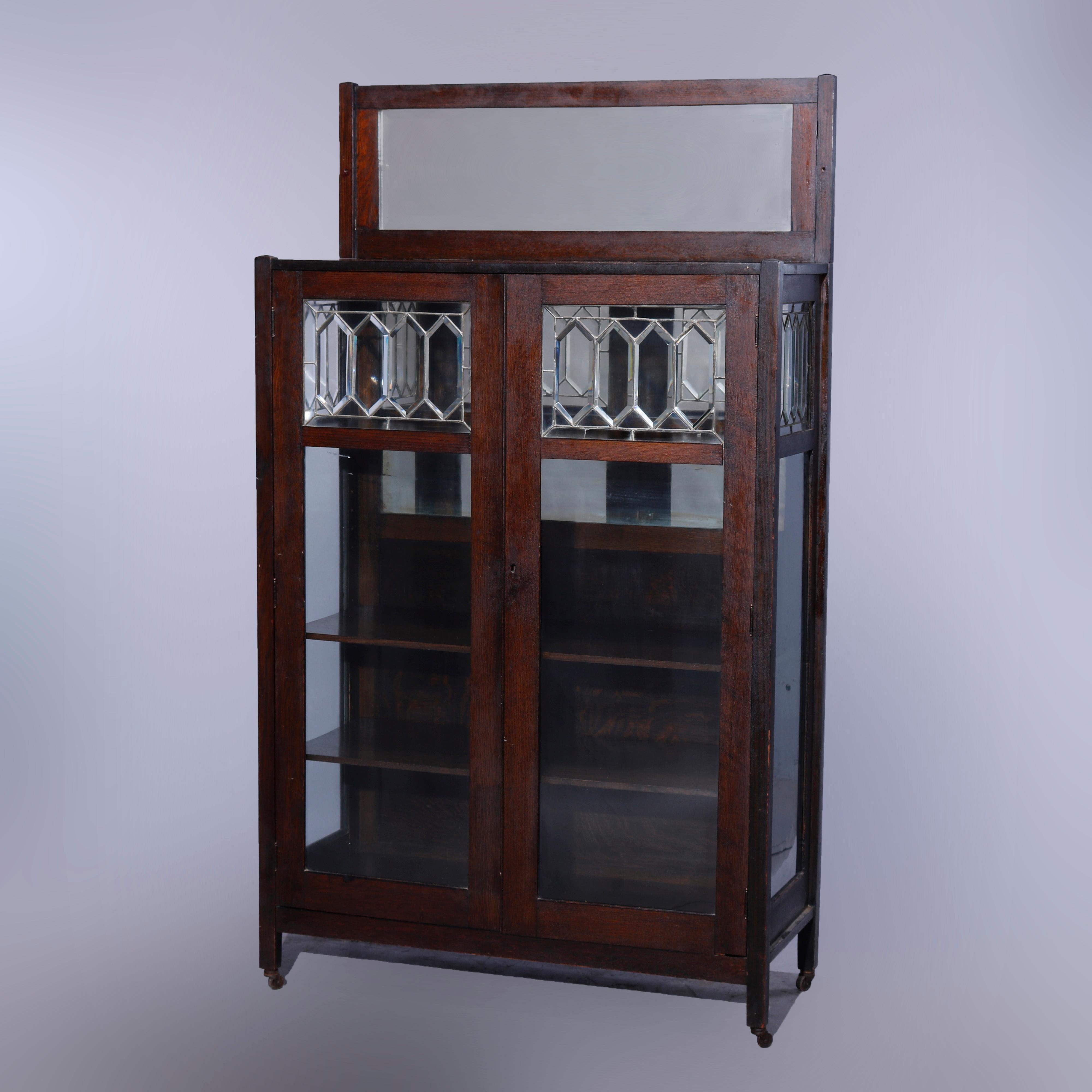 An antique Arts & Crafts mission china cabinet in the manner of Stickley offers quarter sawn oak construction with beveled mirror backsplash surmounting case with double leaded glass doors opening to mirrored and shelved interior, raised on straight