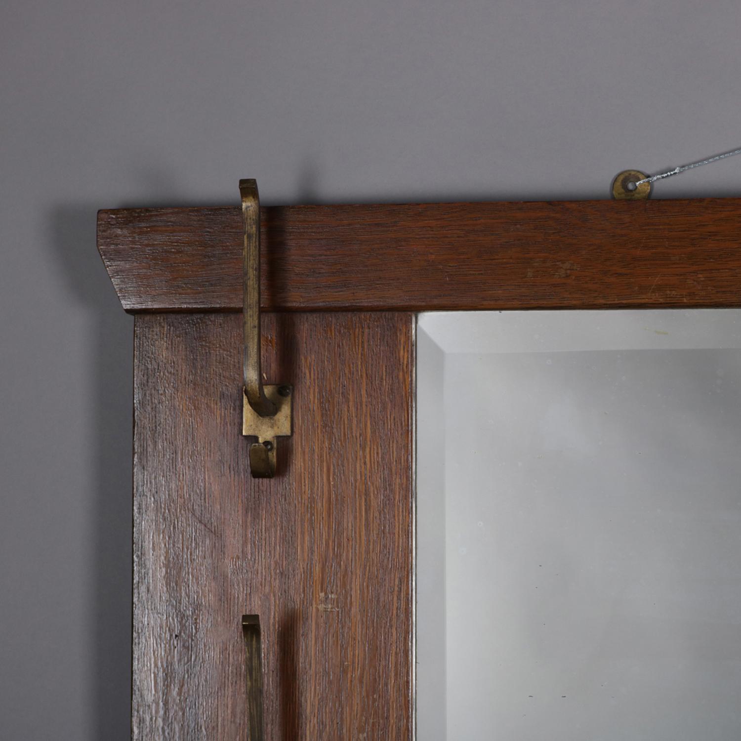 An antique Stickley School Arts & Crafts mission oak wall mirror features beveled mirror with flanking hat hooks and lower garment hooks, circa 1910

Measures - Frame 39